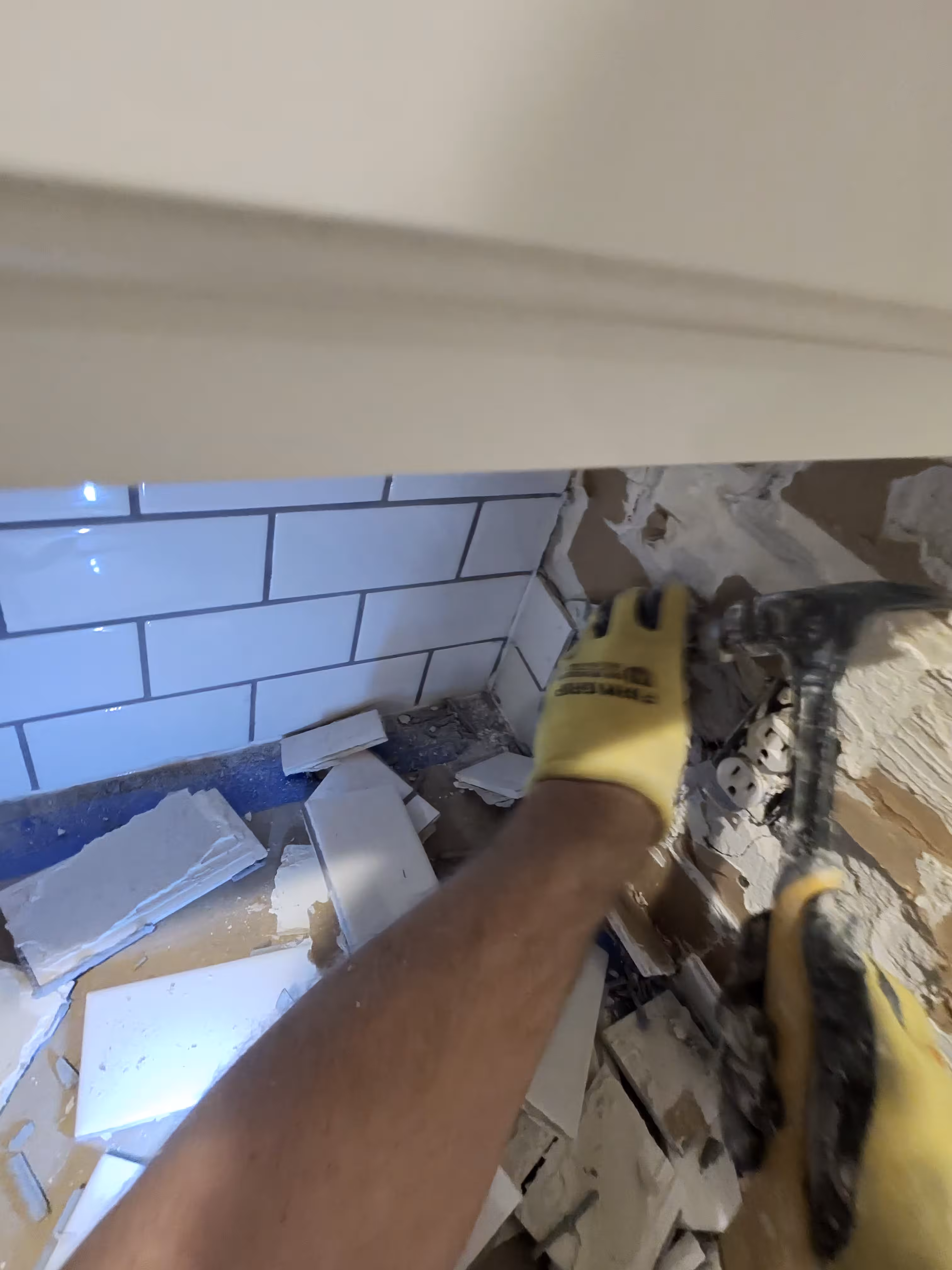 Contractor hammering out cracked old subway tile down to the bare wall during backsplash demolition in an Aurora kitchen