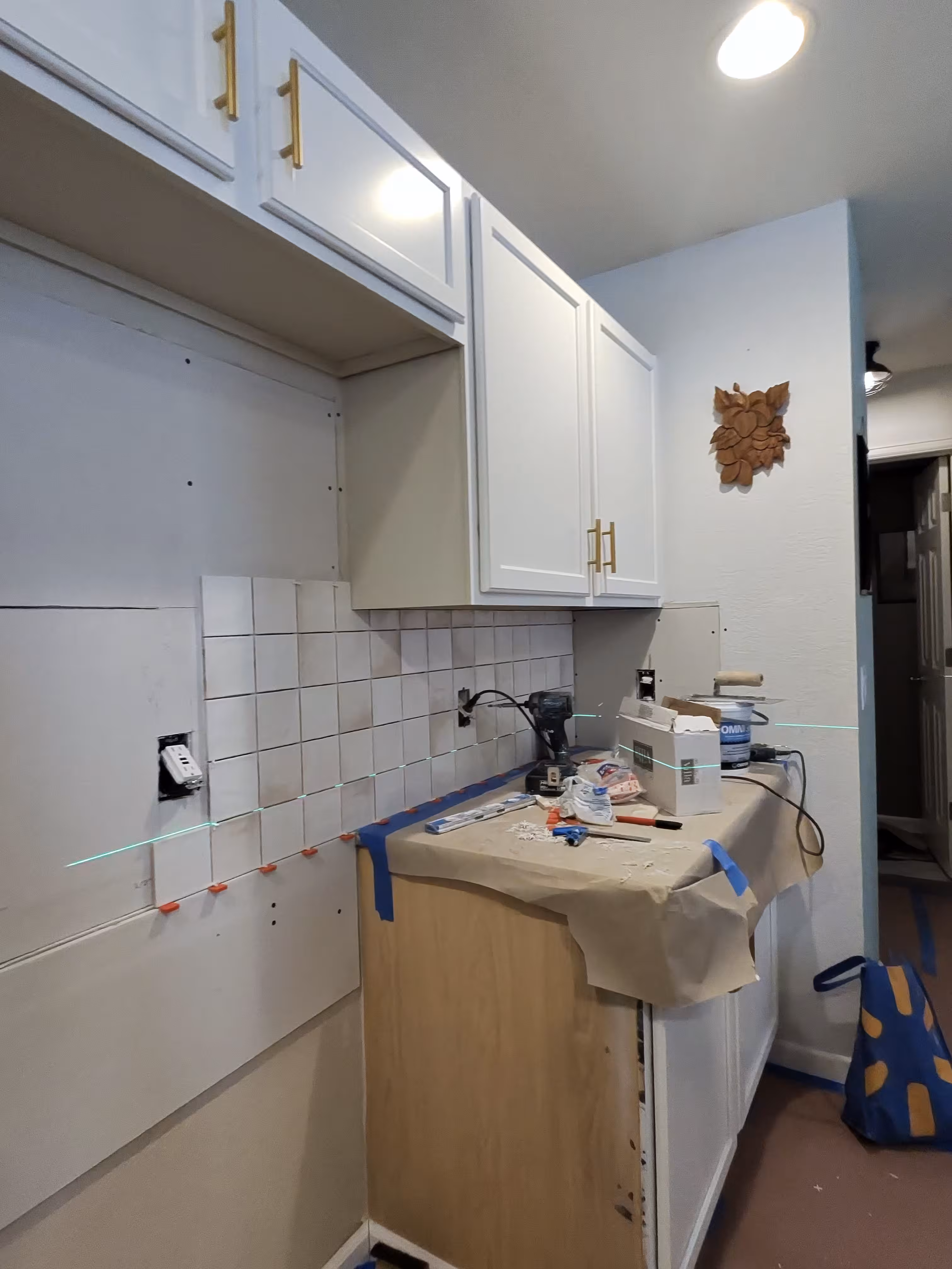 Remaining tan tile backsplash next to a freshly stripped, prepped section of wall mid-demolition in this Aurora kitchen
