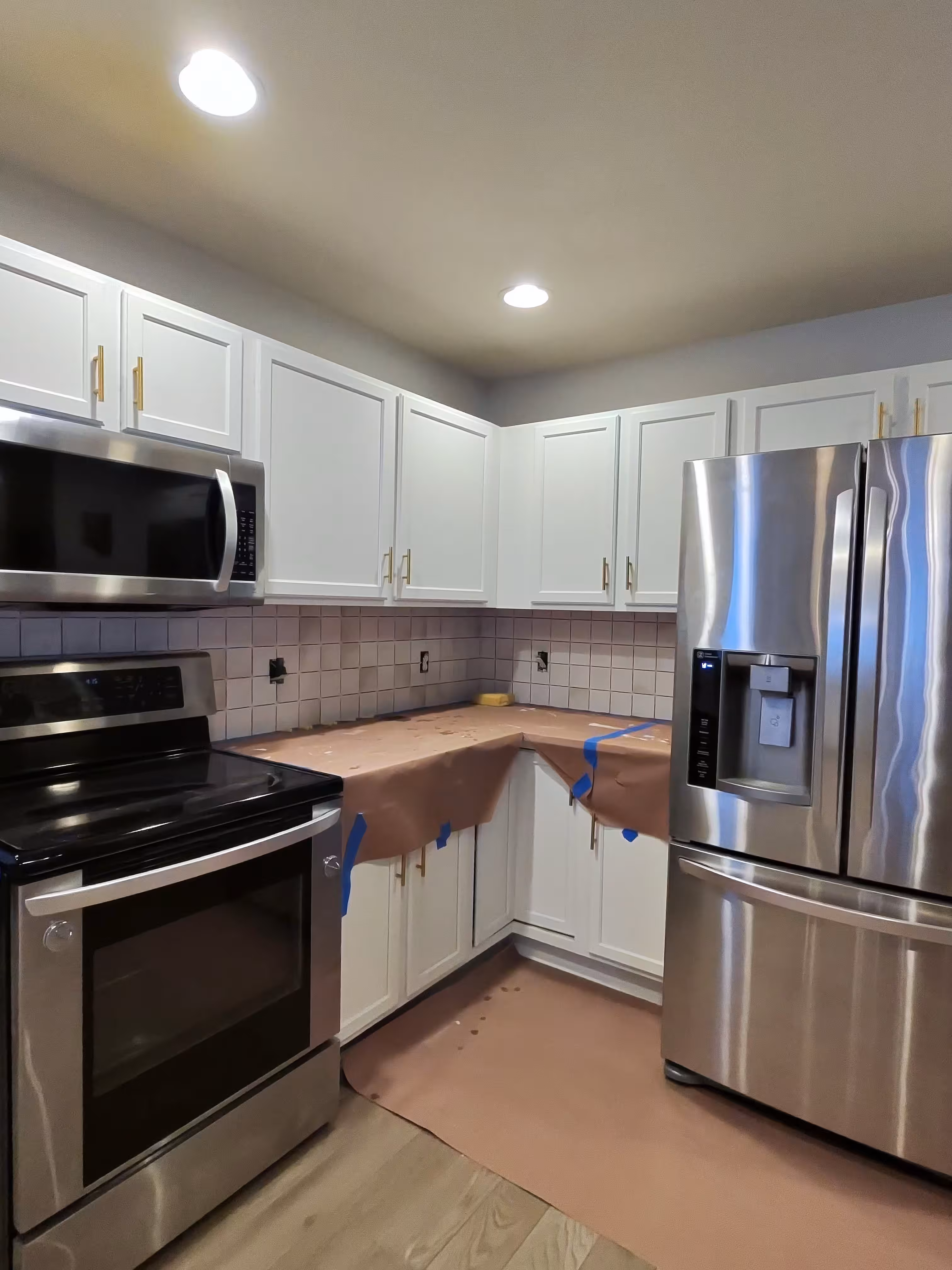 Outdated small tan tile backsplash before this Aurora kitchen remodel, with counters wrapped in protective paper