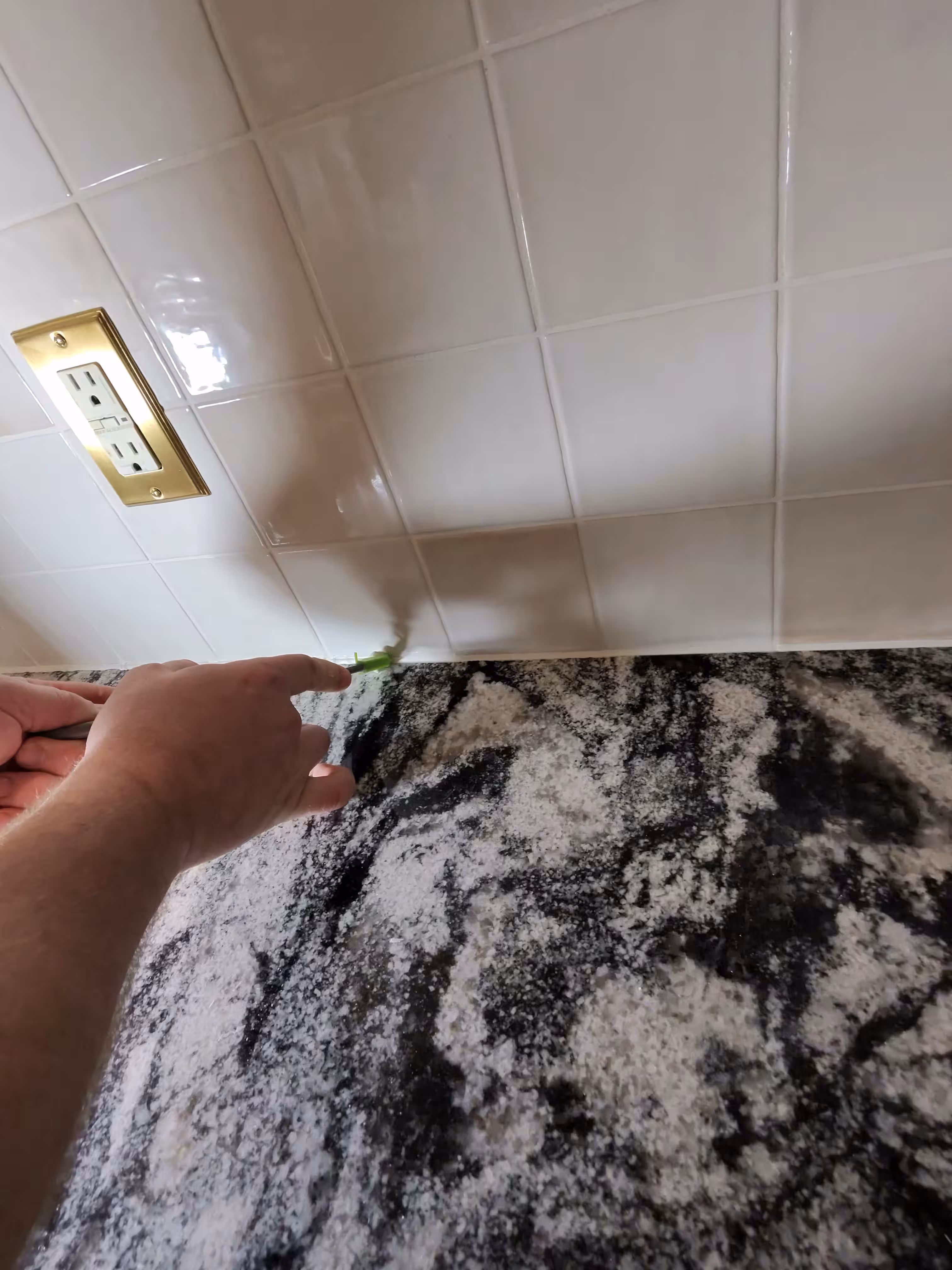 Sealing the seam between glossy white tile and granite countertop with fresh caulk in this Aurora kitchen
