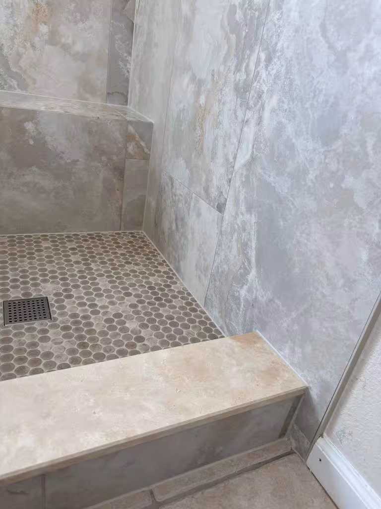 Finished shower threshold and corner with tiled step, penny-tile floor, and marble-look walls in this Highlands Ranch master bathroom remodel