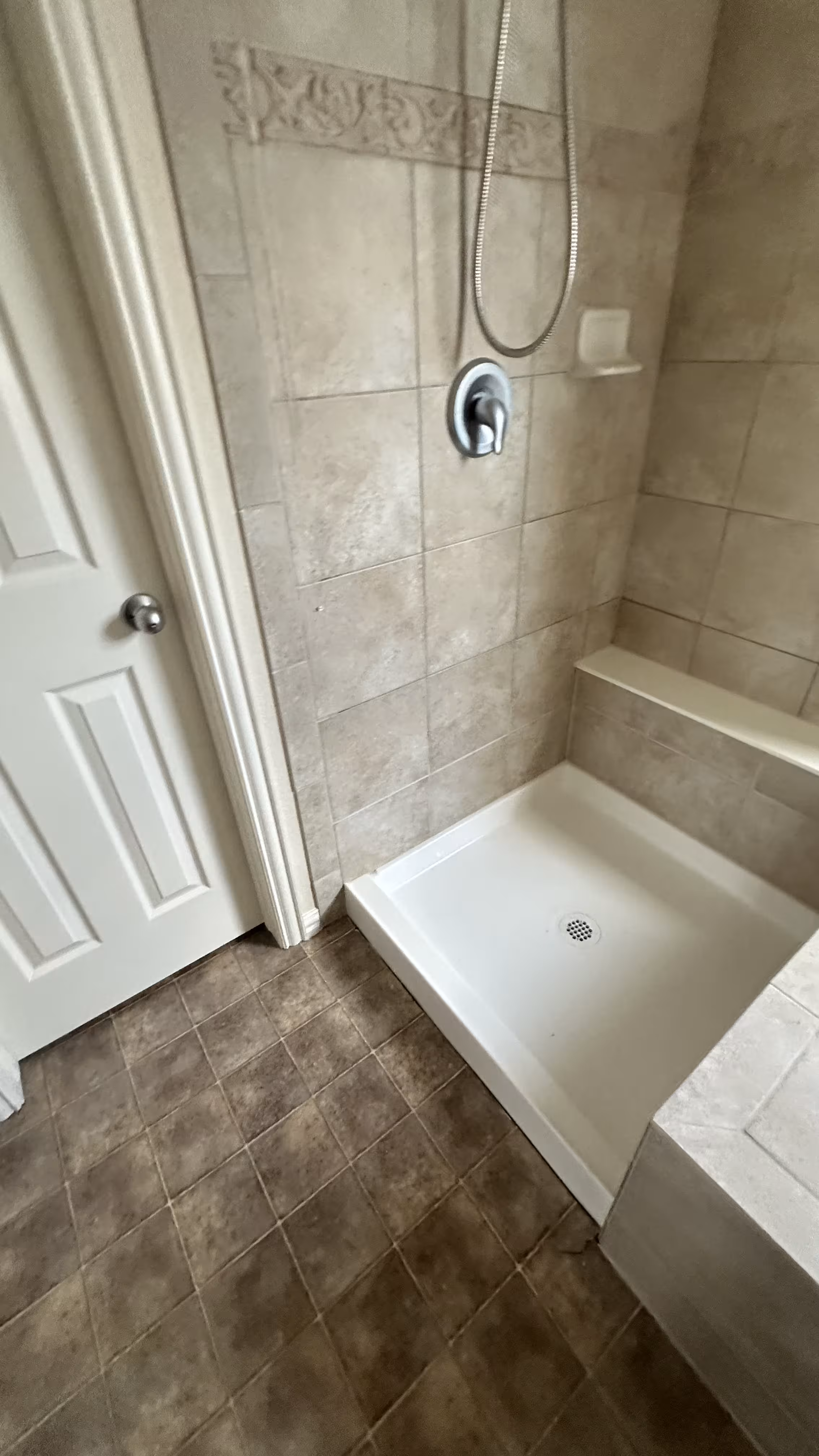 Finished shower alcove with decorative tile accent band and handheld shower head after leak repair in Aurora, CO