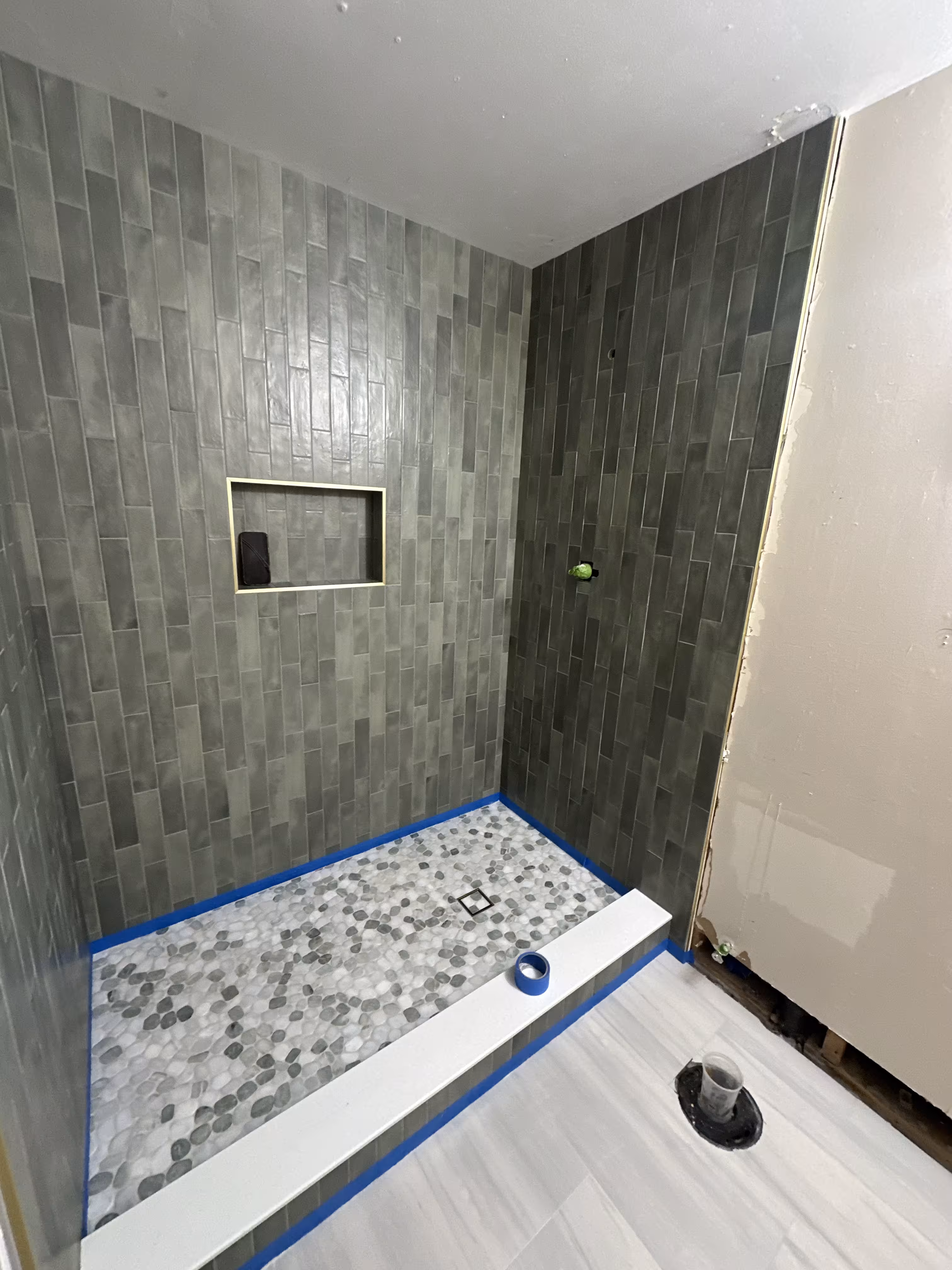 Finished green stacked tile shower with pebble floor and tiled bathroom floor in Commerce City, CO