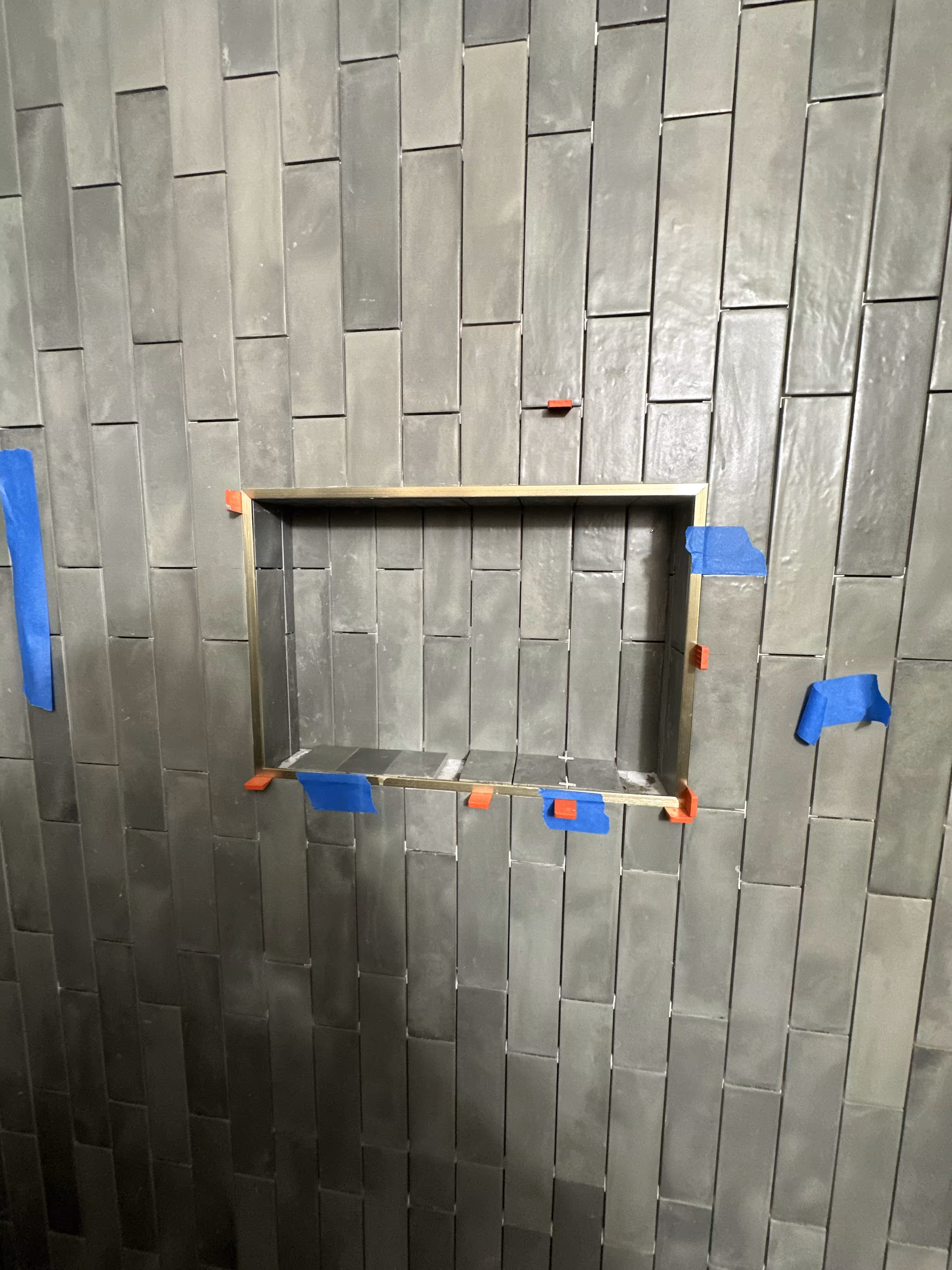 Close-up of the brushed metal niche trim set into the green stacked tile shower wall