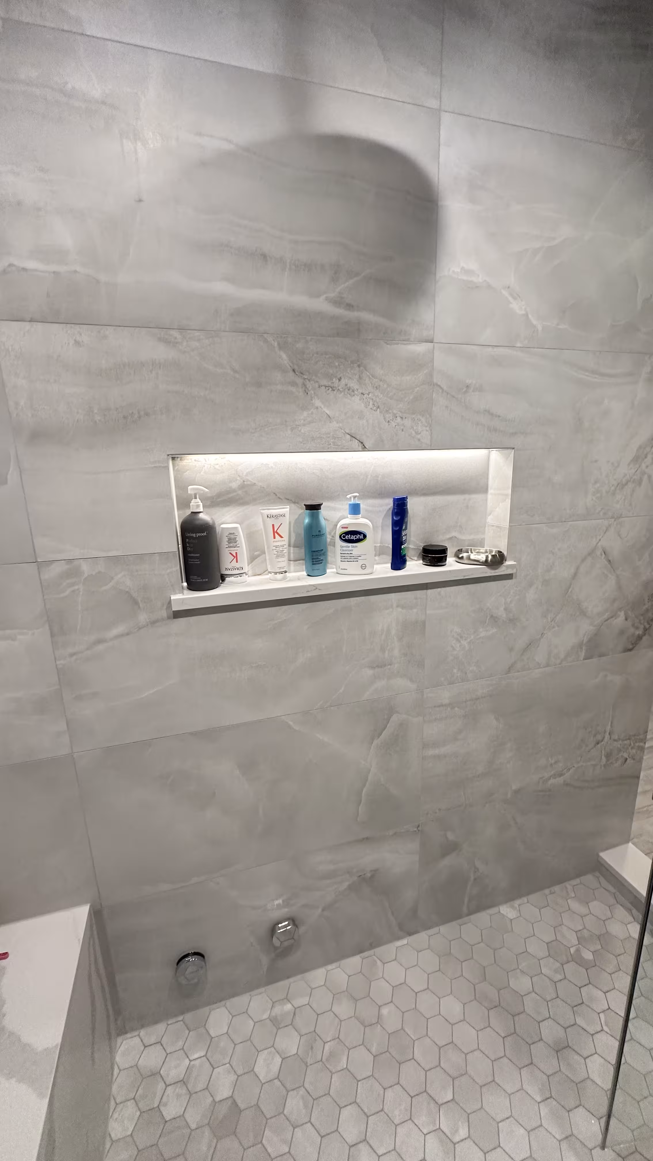 Backlit shower niche stocked with toiletries above a chrome shower valve in a finished Denver steam shower