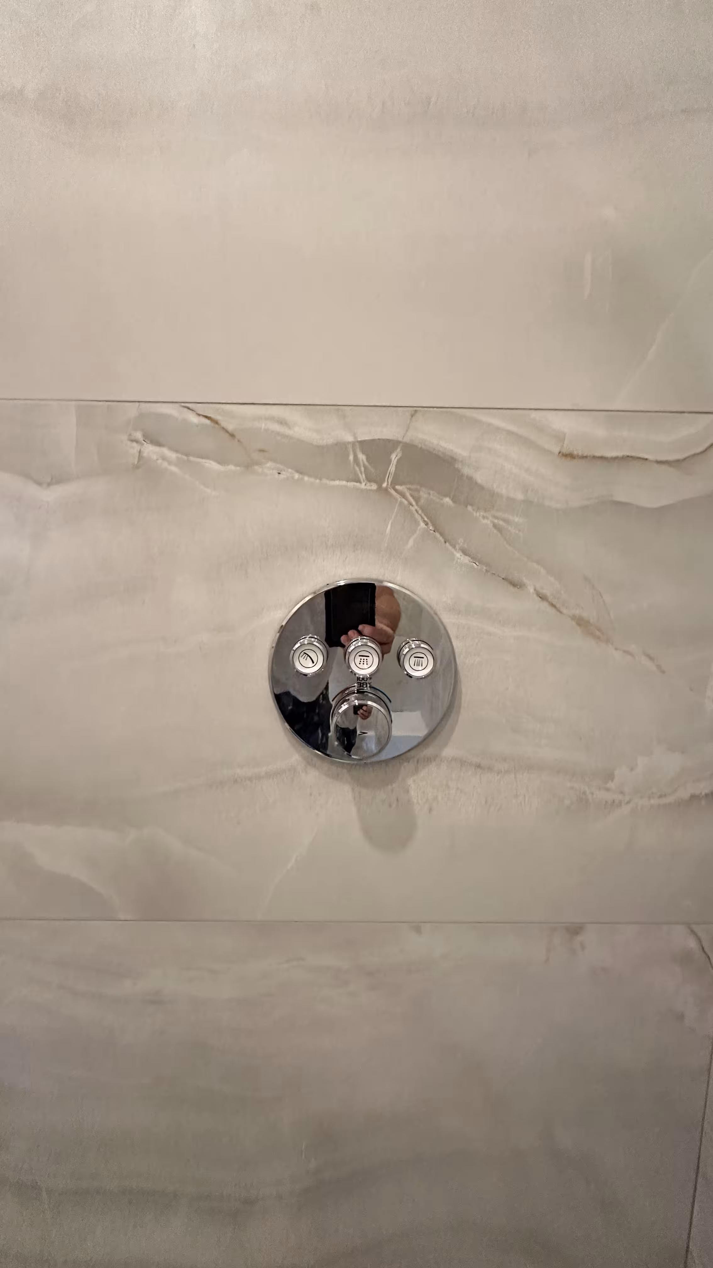 Close-up of a polished chrome thermostatic shower valve with three volume controls set into marble-look tile in Denver, CO