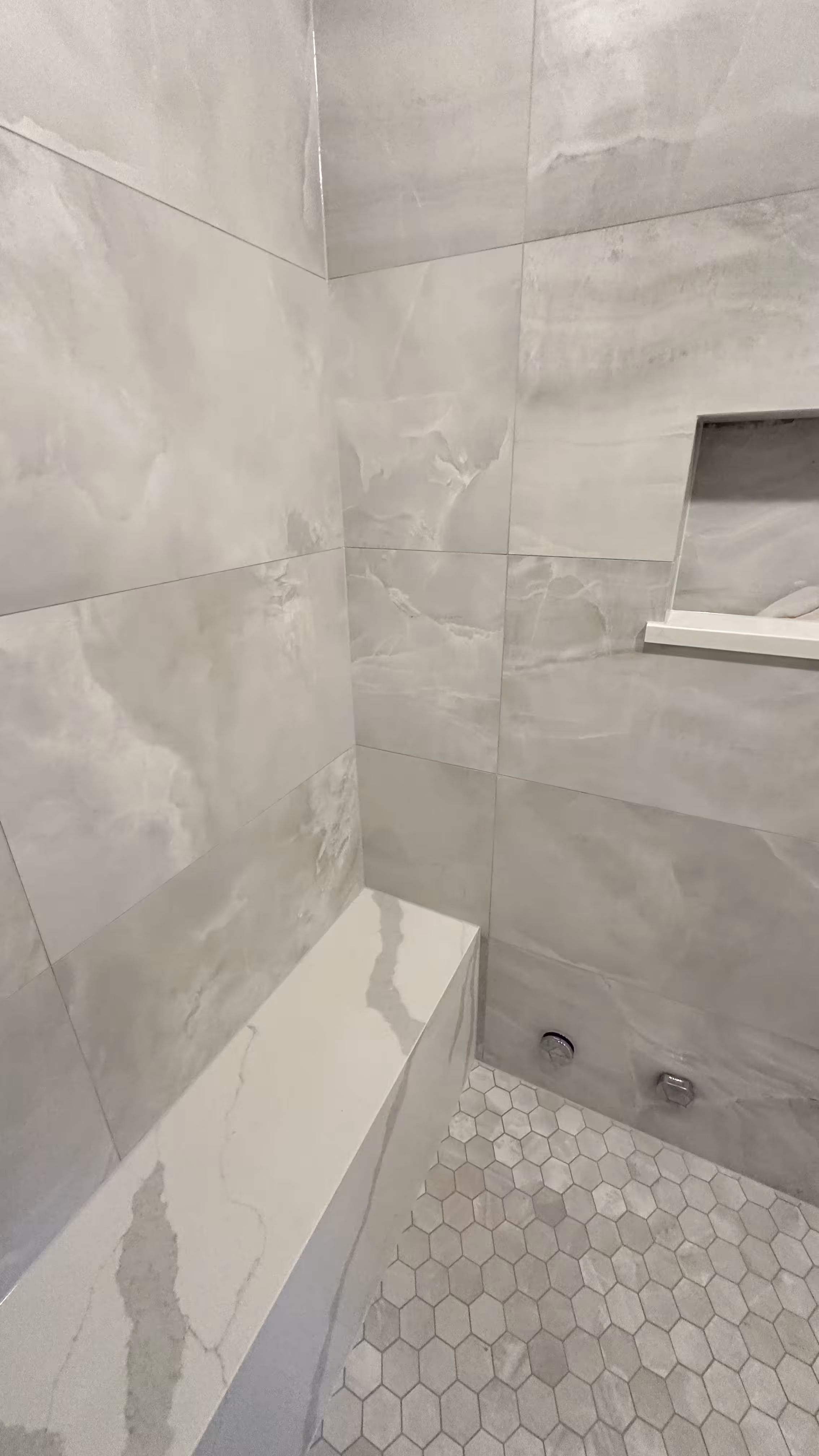 Finished steam shower interior showing the marble-look tiled bench, recessed niche, and hexagon mosaic floor with chrome body sprays in Denver, CO