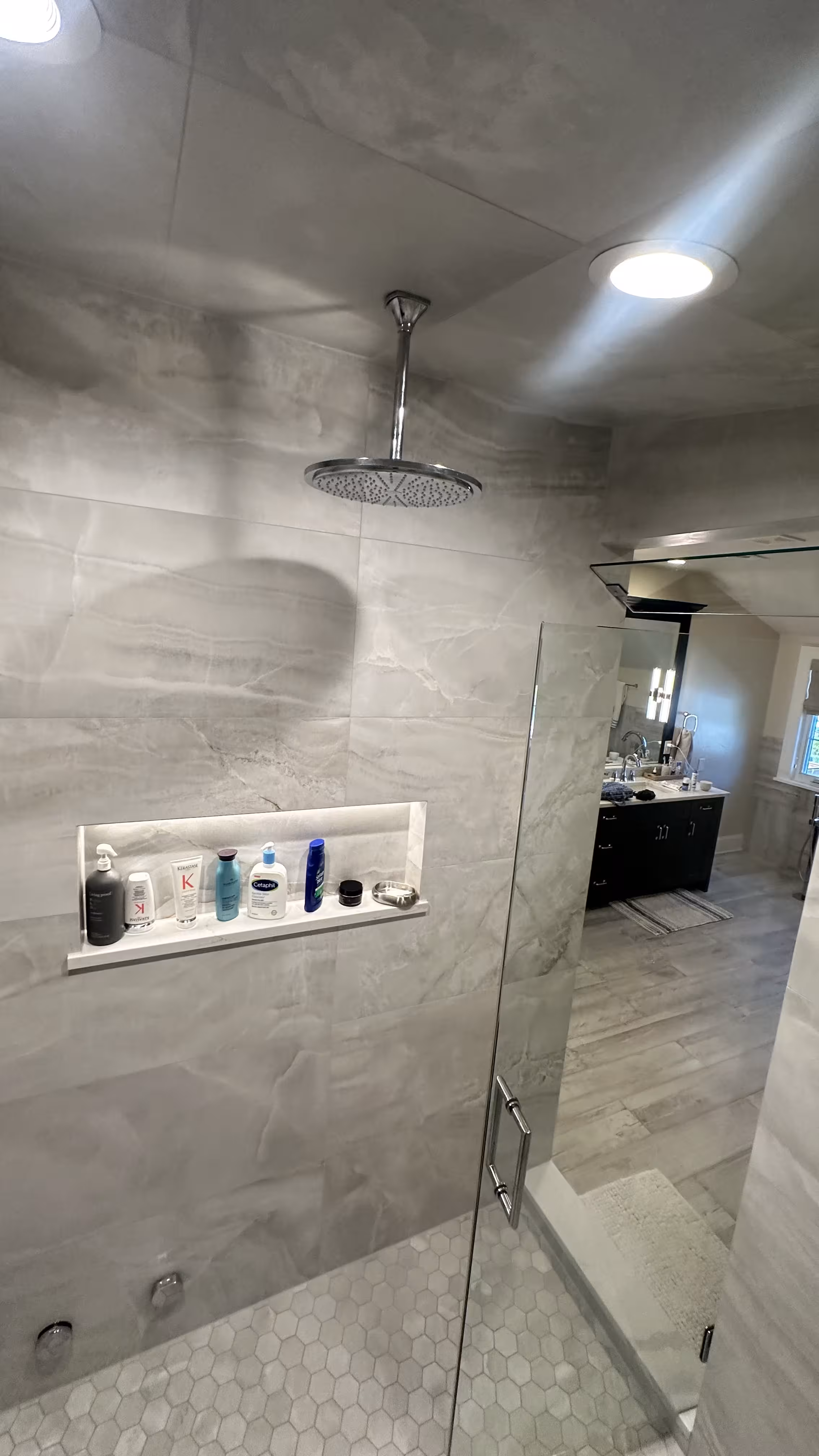 Finished Denver steam shower with ceiling rain head, backlit niche, and open glass door revealing the ensuite vanity beyond