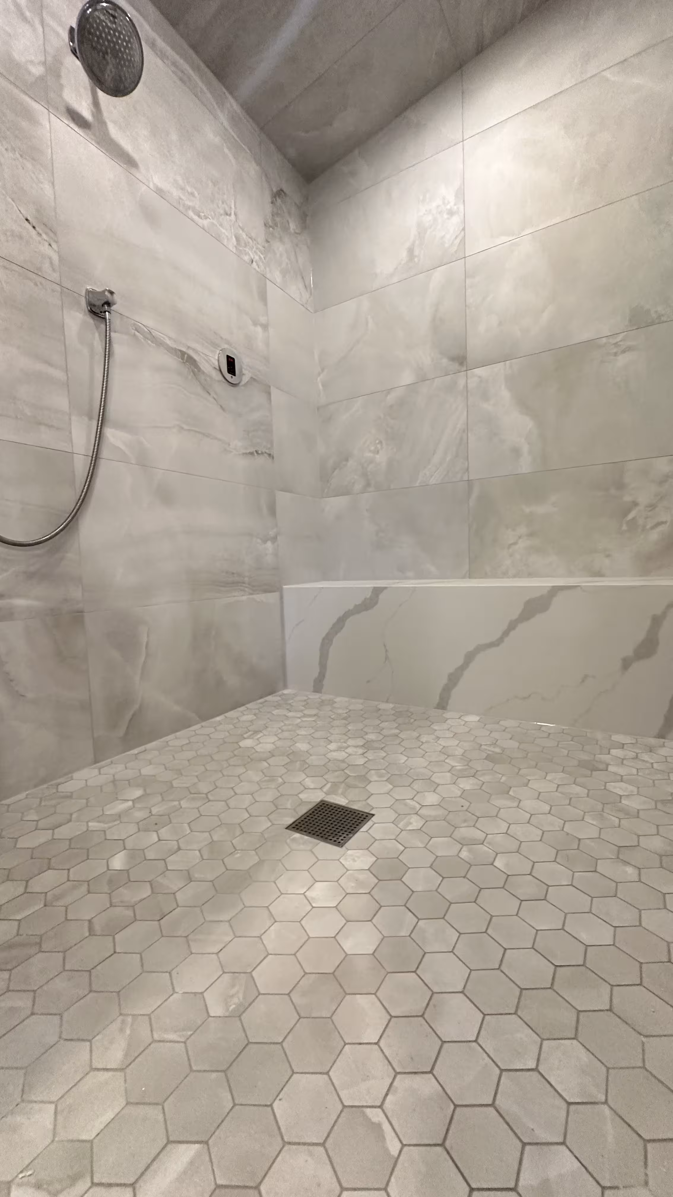 Finished Denver steam shower corner showing the ceiling rain head, marble-look bench, and hexagon mosaic floor with drain
