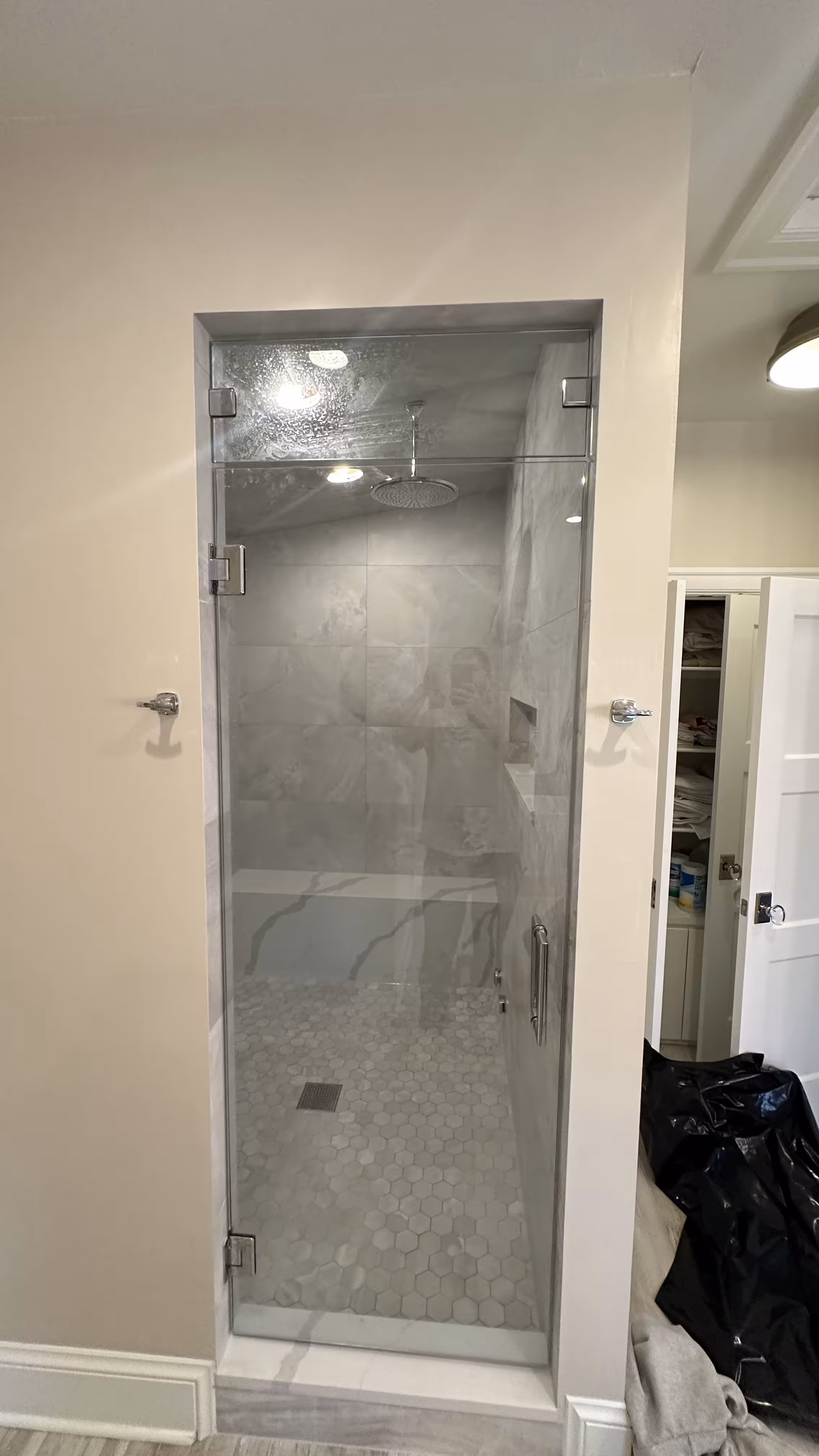 Finished frameless glass steam shower enclosure with chrome hardware, marble-look tile, and hexagon mosaic floor in a Denver bathroom