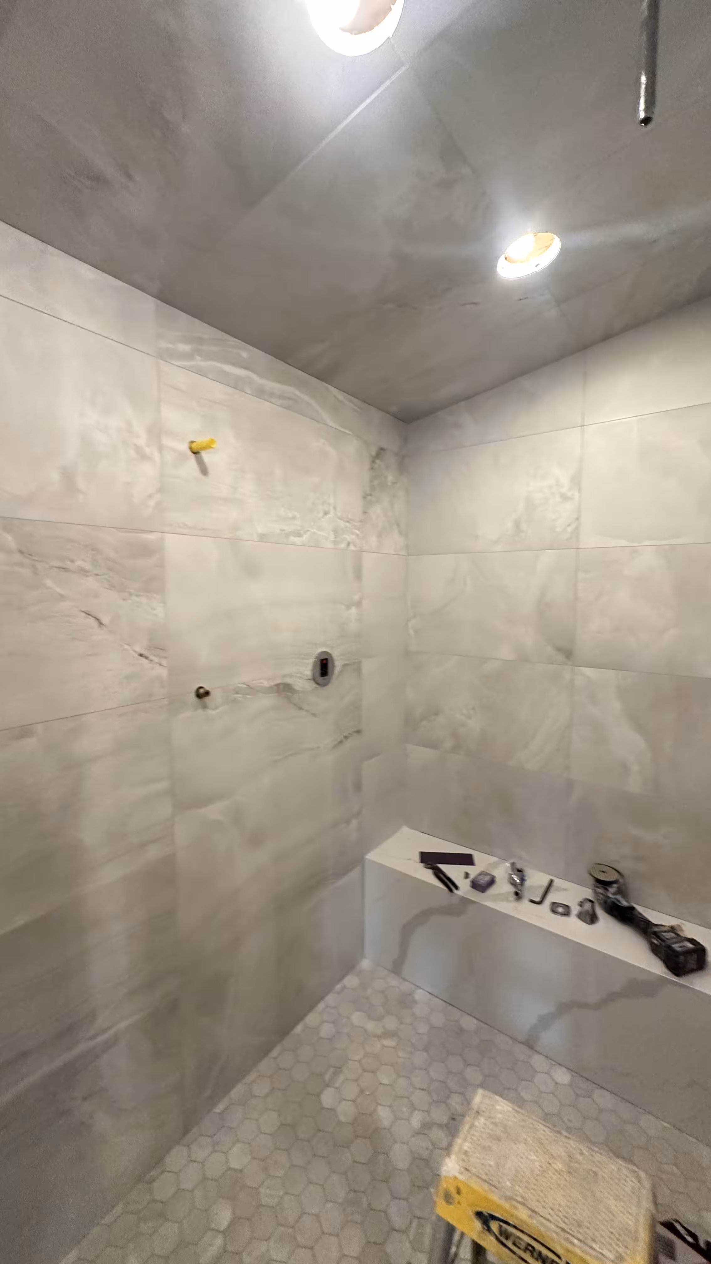 Freshly grouted marble-look porcelain walls in a steam shower with a capped plumbing stub awaiting the valve trim in Denver, CO