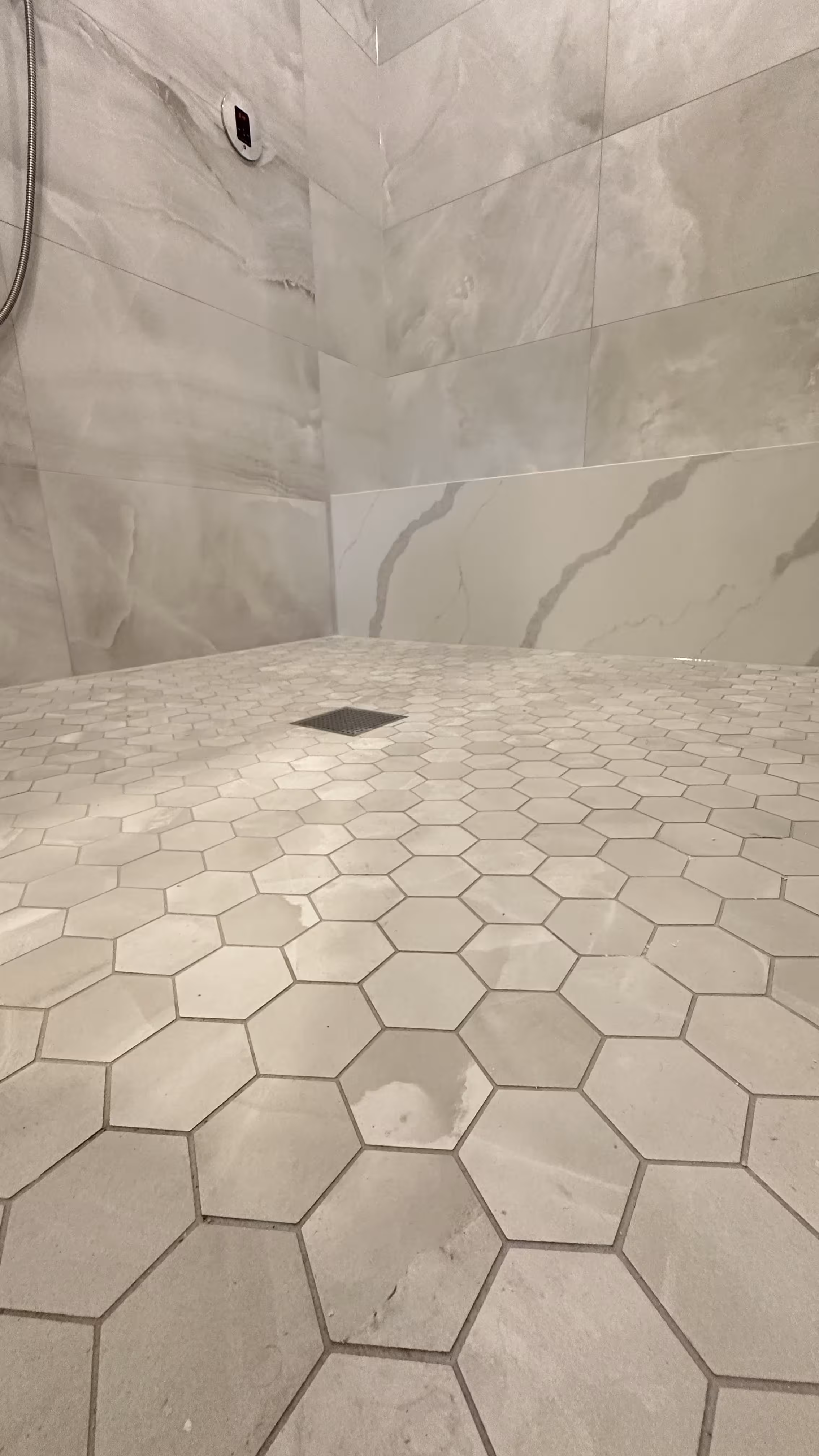 Close-up of the marble-look hexagon mosaic shower floor and square drain in a finished Denver steam shower