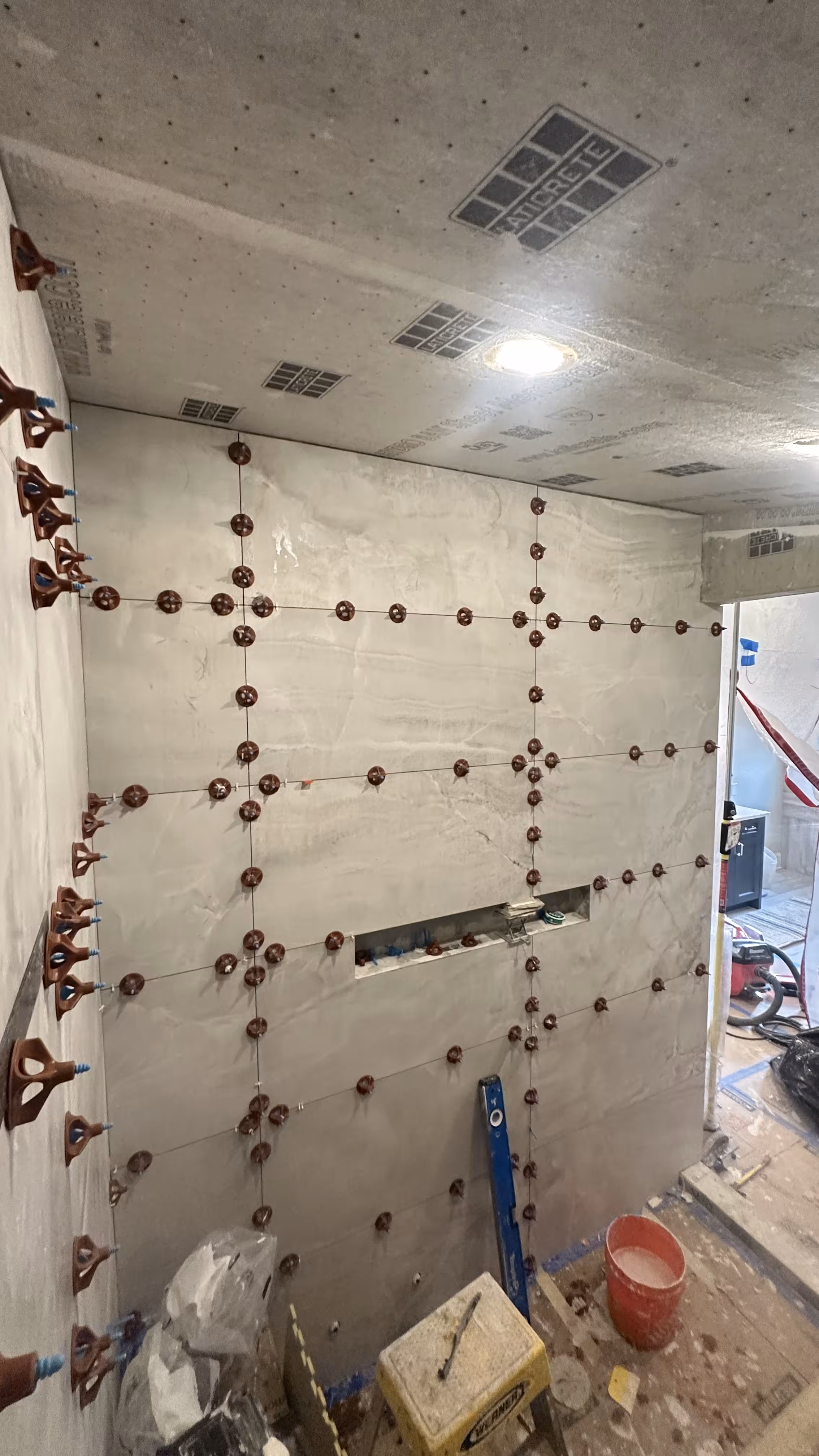 Close view of tile leveling clips holding large-format marble-look porcelain tile flush on a steam shower wall in Denver, CO