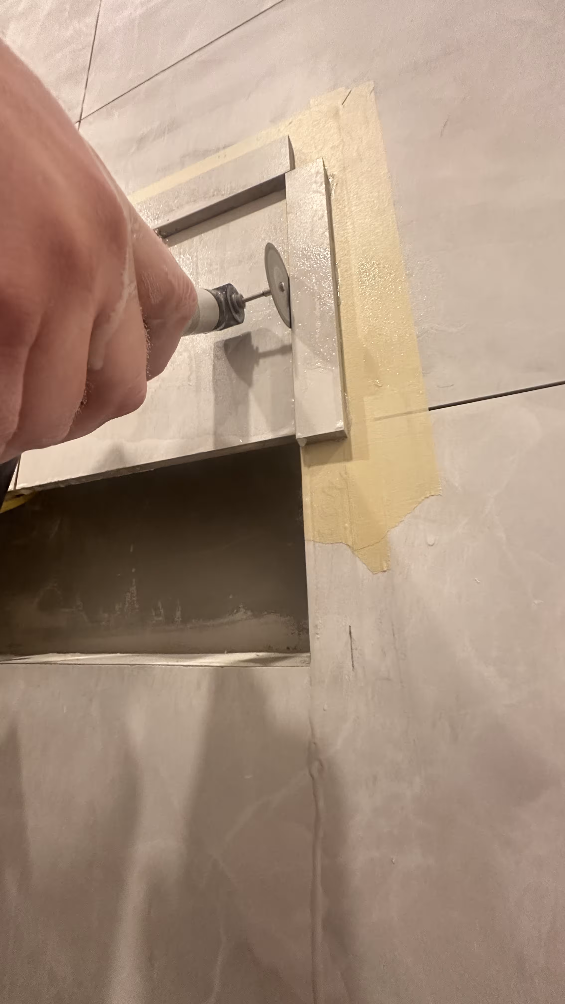 Tile installer grinding a 45-degree miter on a marble-look porcelain niche corner with a diamond blade in a Denver steam shower