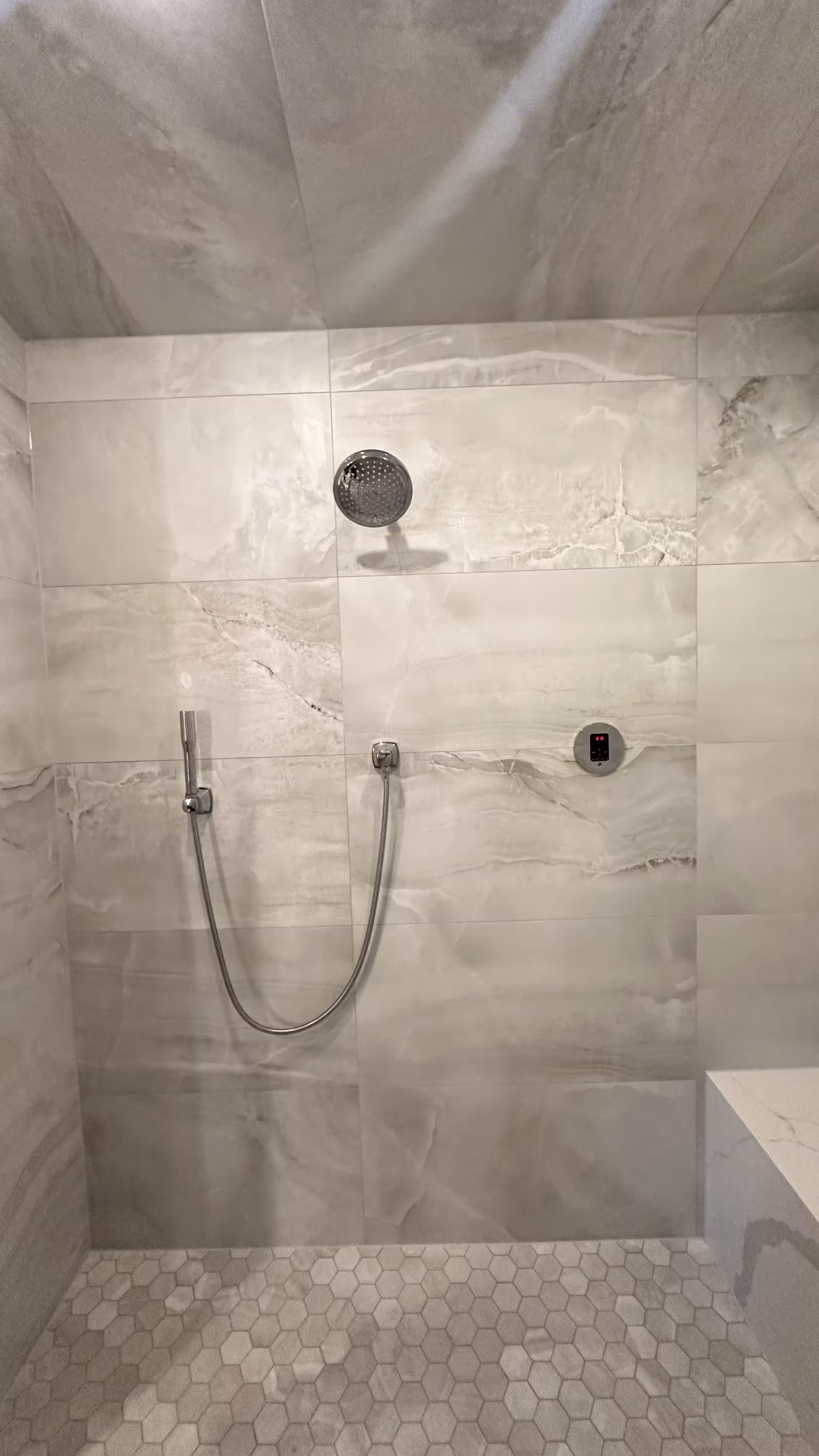 Steam shower wall with rain head, chrome hand shower, and steam generator control keypad above the marble-look bench in Denver, CO