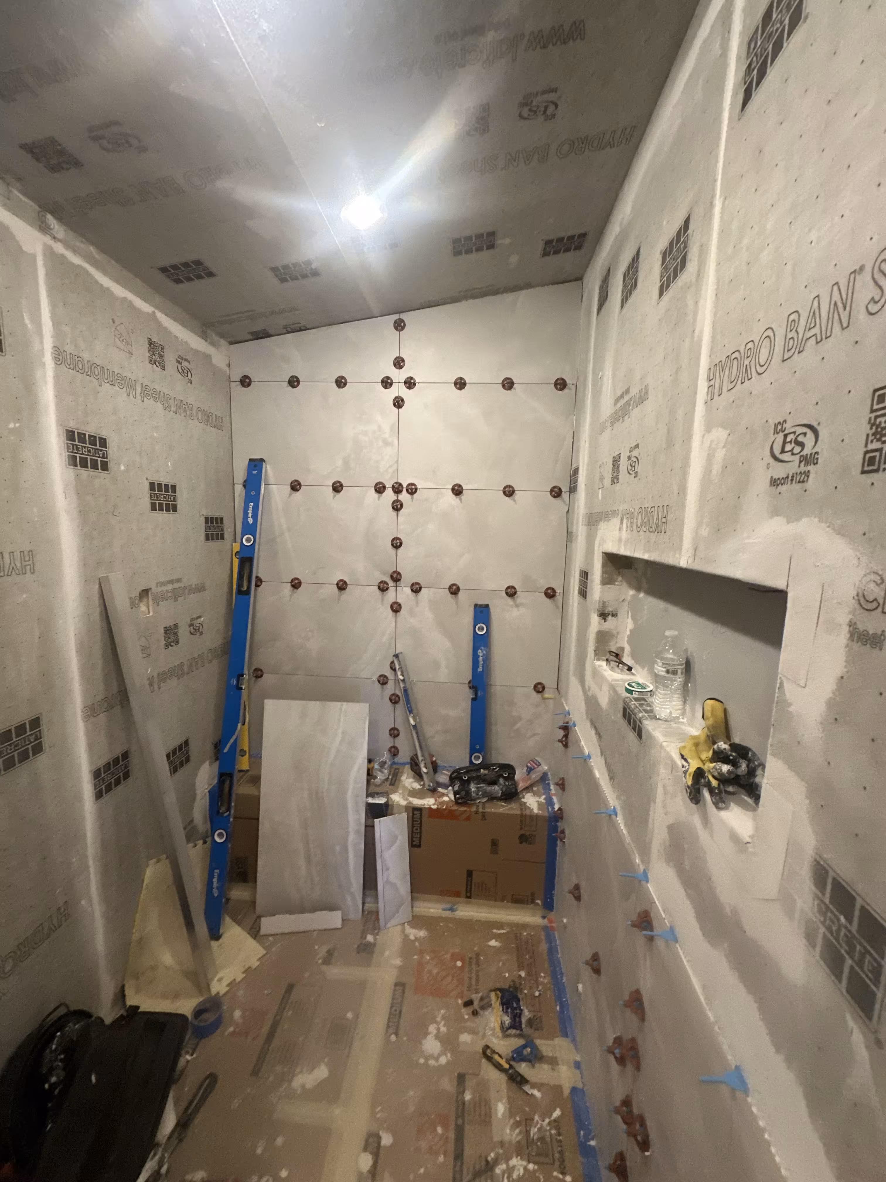Waterproofed steam shower walls with tile leveling clips and layout lines marking the large-format tile grid before installation in Denver