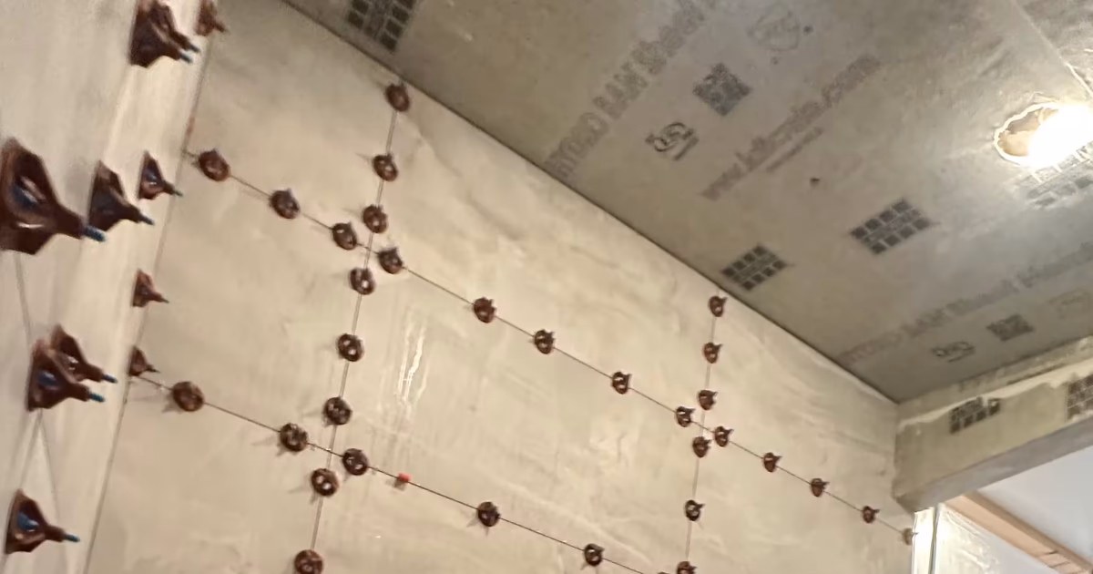 Steam shower wall mid-installation in Denver with a grid of tile leveling clips holding large-format marble-look porcelain tile flush, with a ladder and mortar bucket
