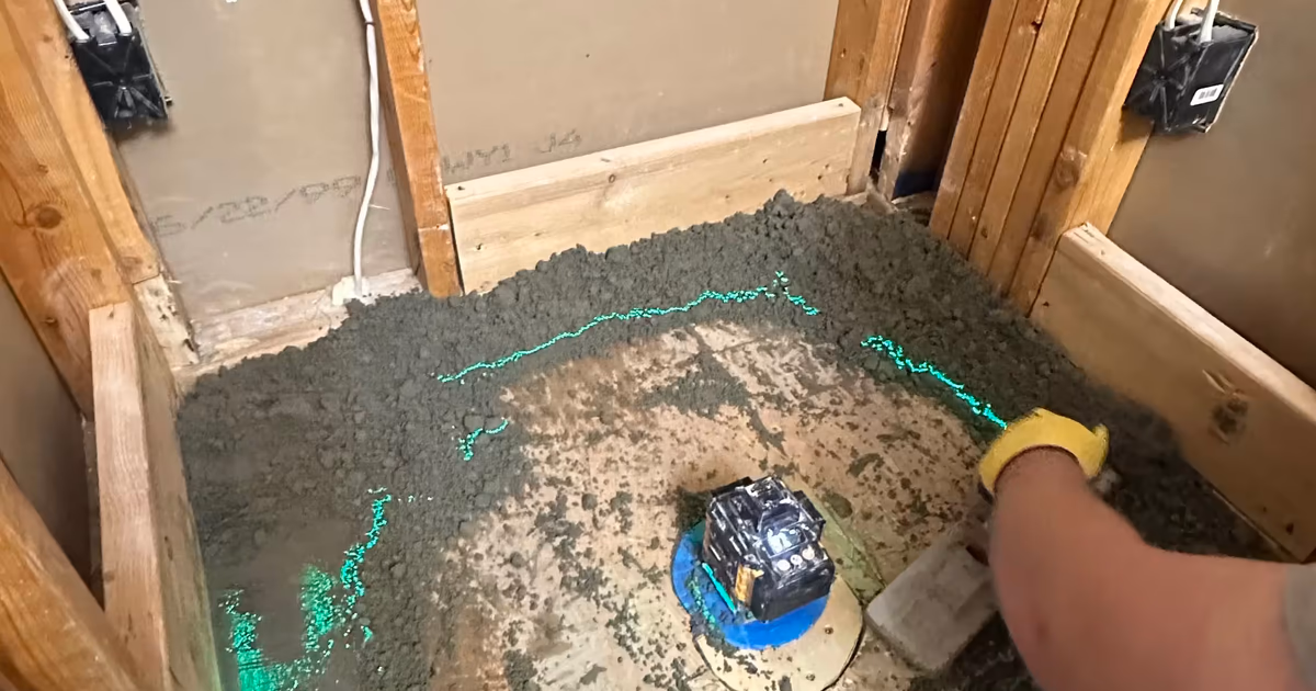 New shower drain set in a freshly floated mortar pre-slope, with open wall framing, electrical boxes and wiring still exposed, during a Highlands Ranch master bathroom remodel