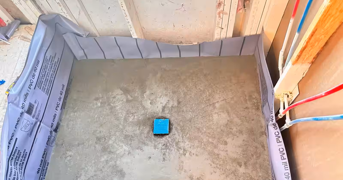 Shower pan in Commerce City at the waterproofing stage, before any tile: 40-mil PVC liner turned up the walls, a mortar bed and a covered drain