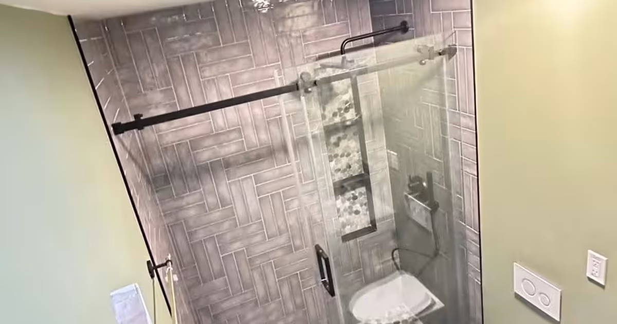 Small Littleton bathroom with a walk-in shower behind a sliding glass door and herringbone wall tile