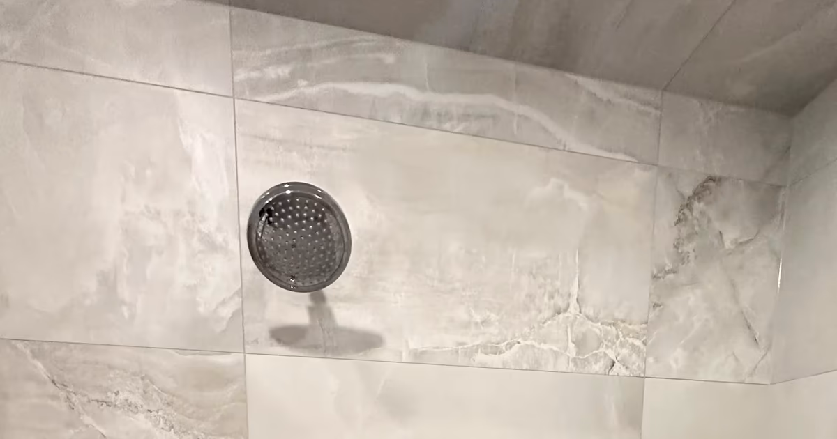 Finished Denver steam shower corner with a mitered marble-look porcelain tile edge below the ceiling rain head