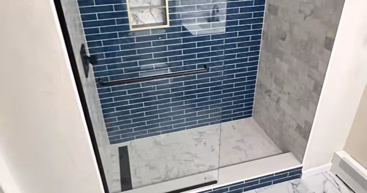 Walk-in shower with a frameless glass panel, linear drain, blue subway tile accent wall and gold-trimmed niche after a basement bathtub-to-shower conversion in Aurora, CO