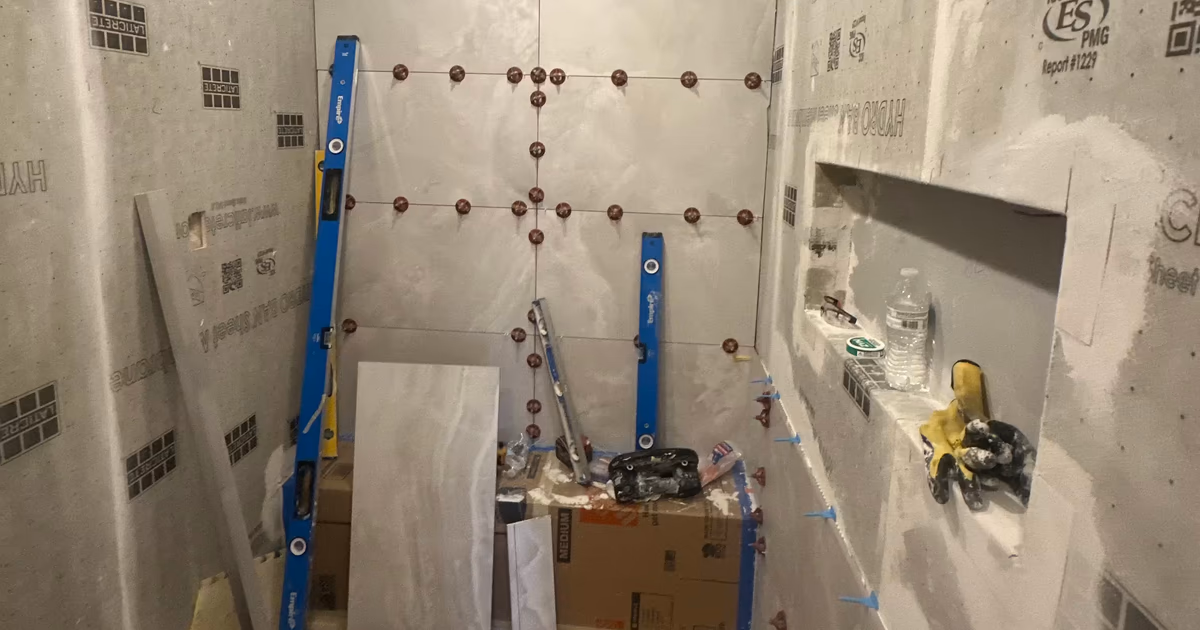 Waterproofed steam shower walls with tile leveling clips and layout lines marking the large-format tile grid before installation in a Denver bathroom