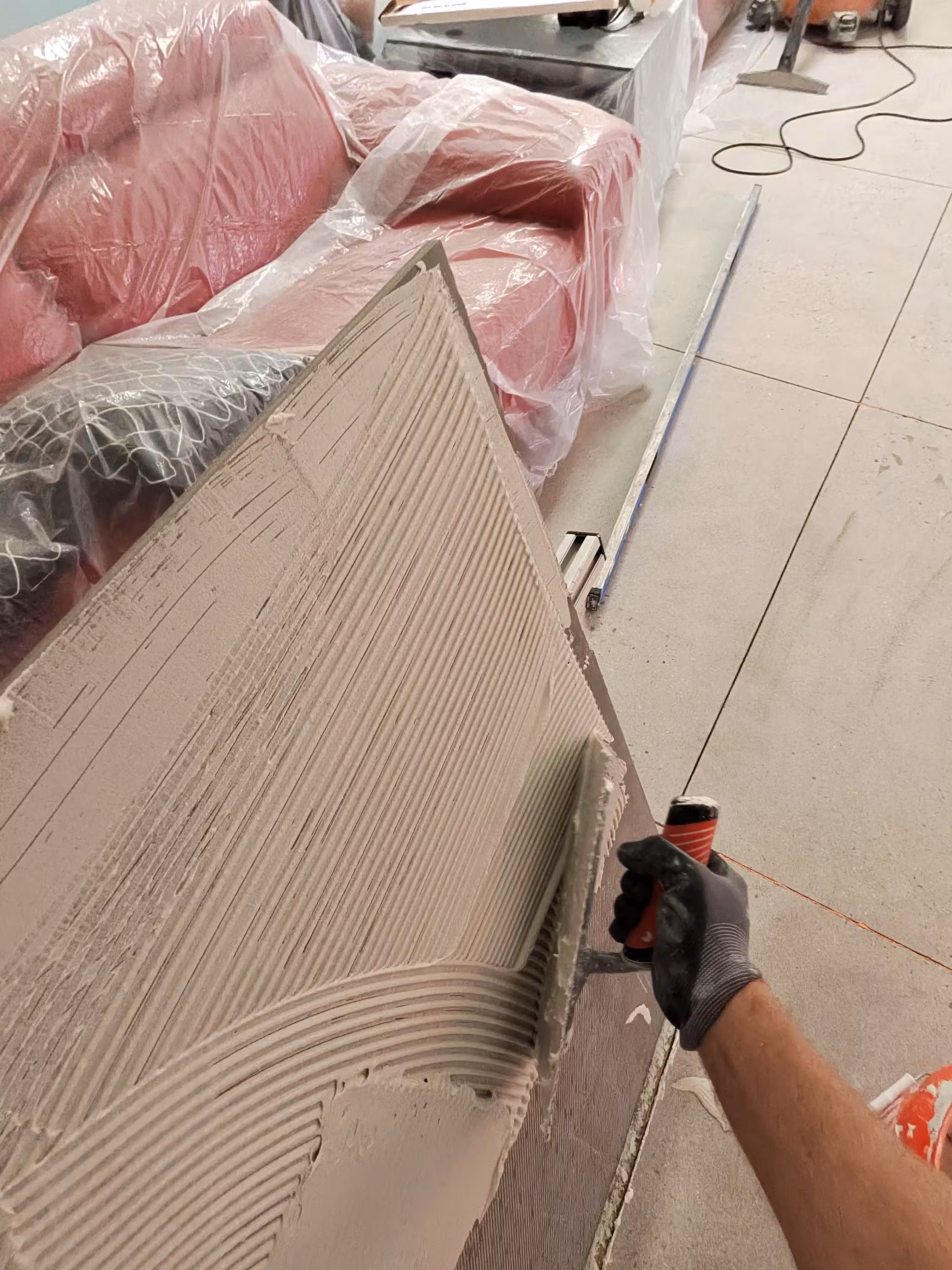 Troweled thinset on the floor and a back-buttered large-format tile during a Denver hallway installation