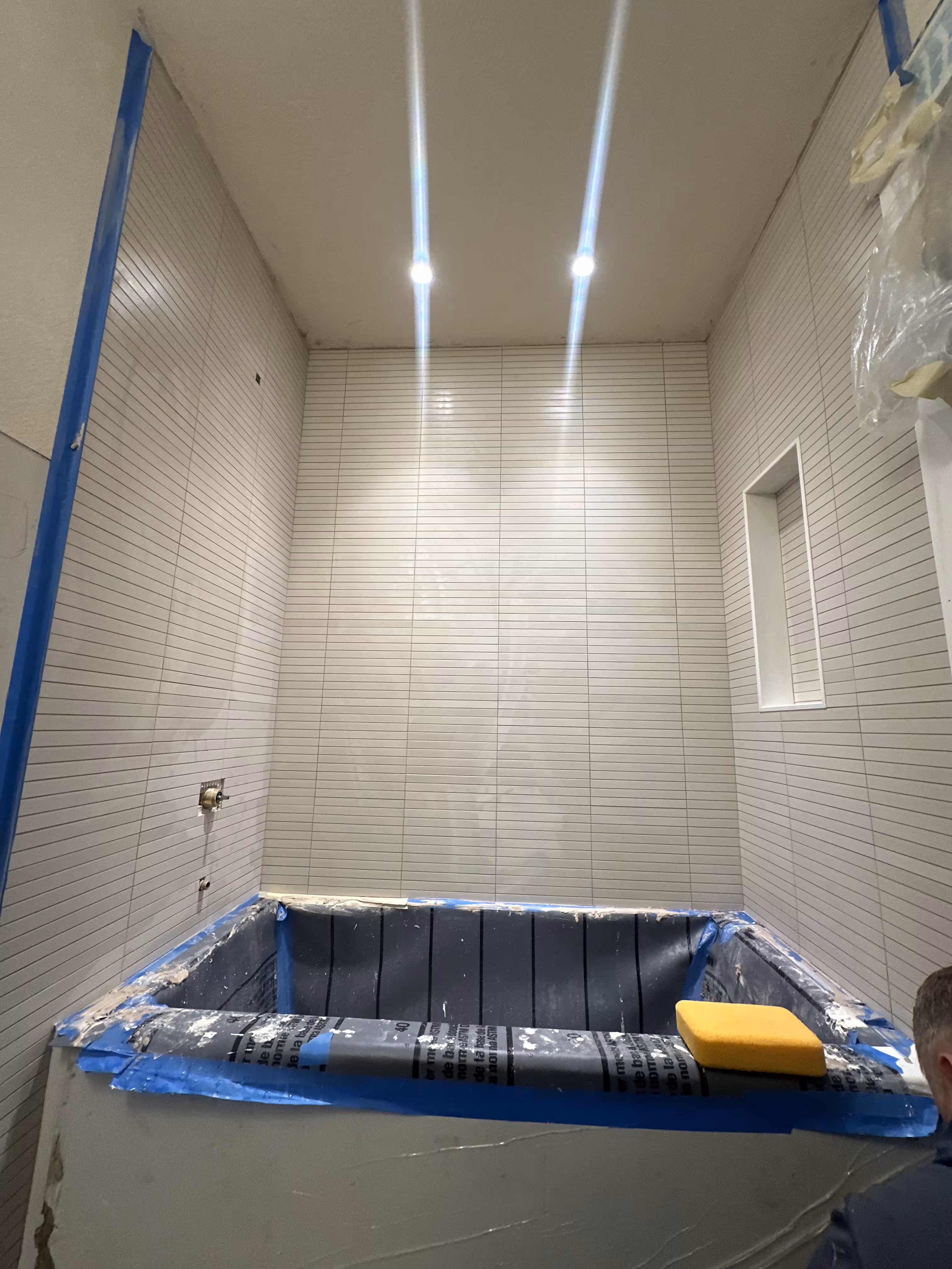 Grout sponge cleanup on white kit-kat mosaic wall tile above a masked alcove tub in Arvada, CO