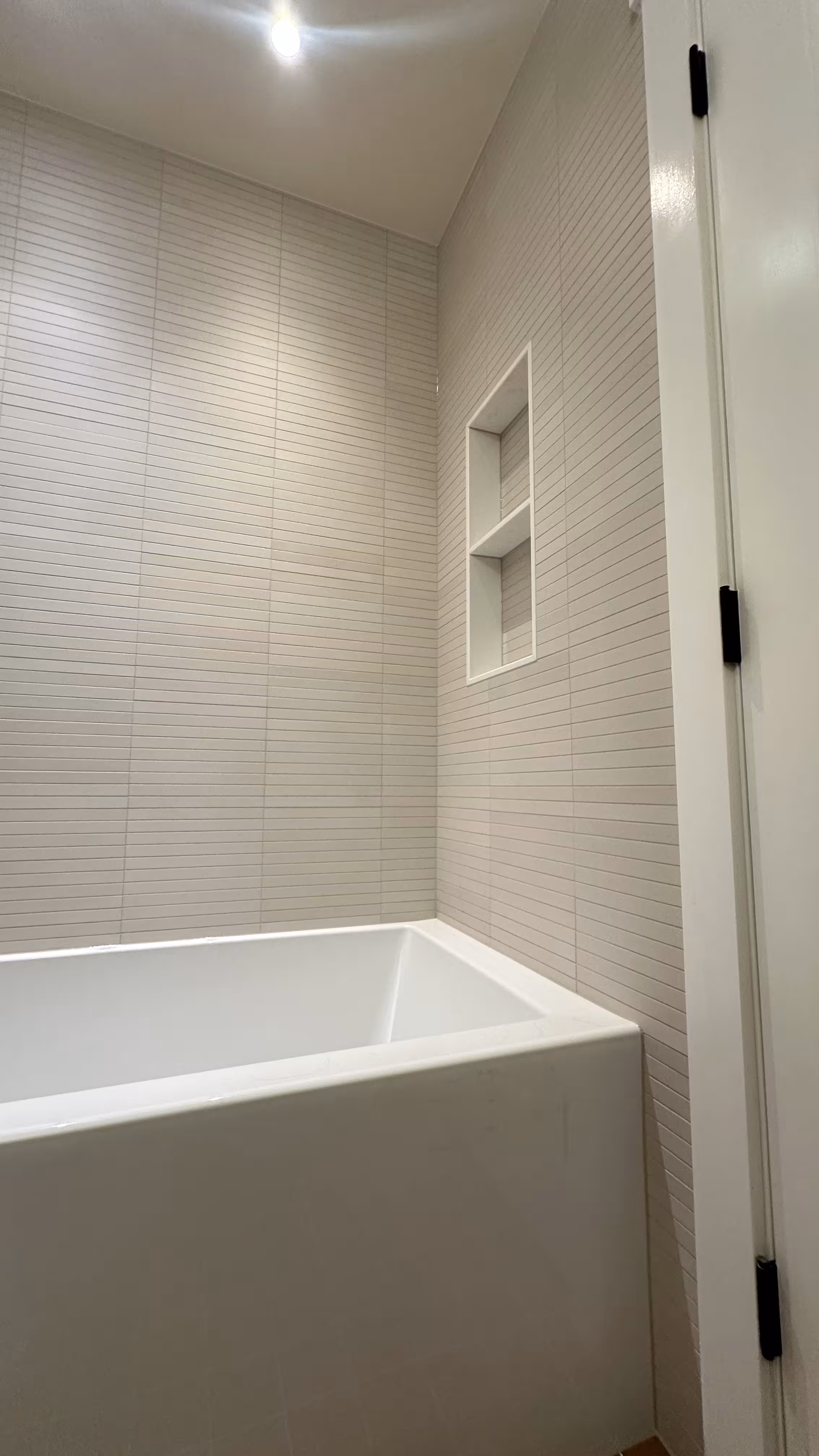 Corner view of the tiled shower niche and alcove tub soon after tiling in this Arvada bathroom remodel