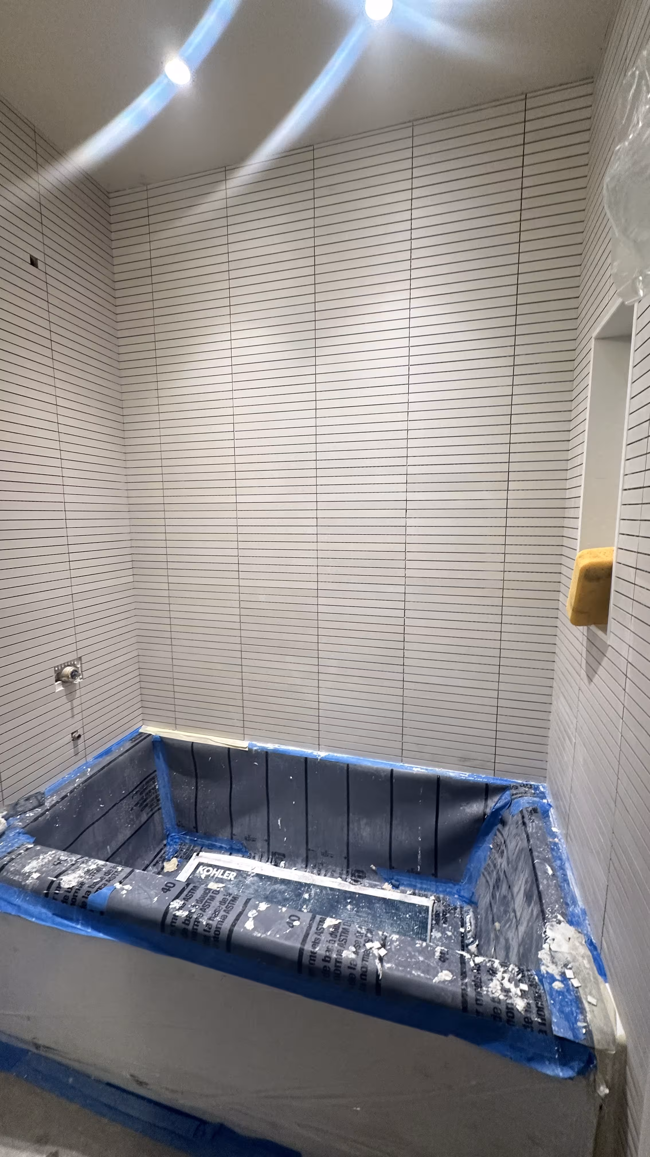 Freshly set white kit-kat mosaic tile surrounding an alcove tub, protected during an Arvada bathroom remodel
