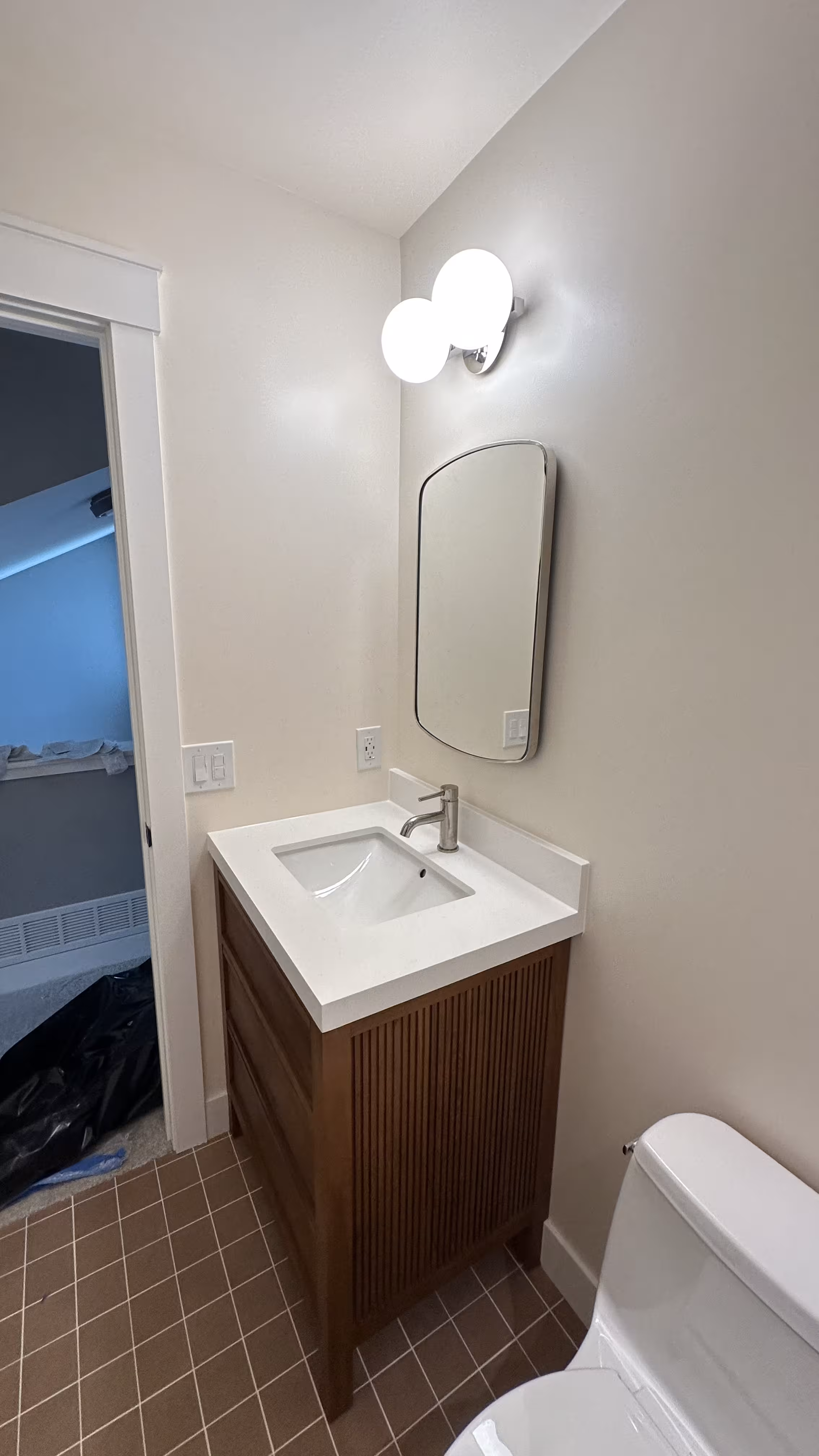 Finished fluted wood vanity, round mirror, and terracotta floor tile in an Arvada bathroom remodel