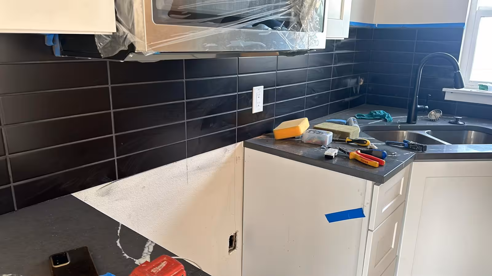 In-progress view of black subway tile kitchen backsplash installation in Denver home
