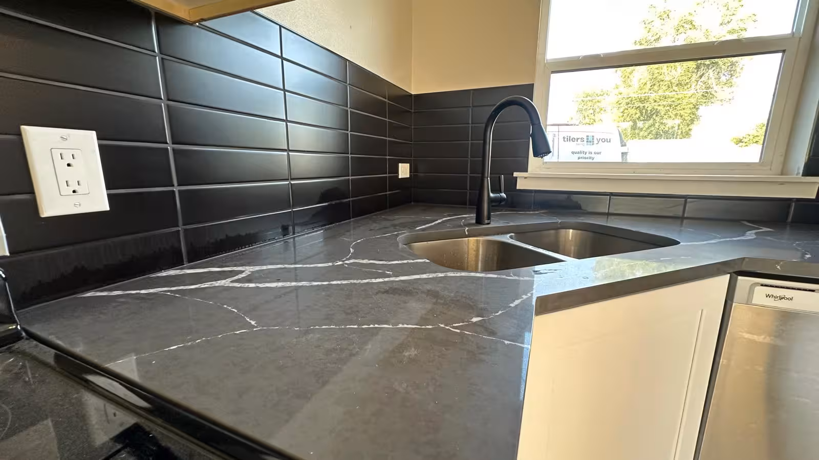 Kitchen sink area showing black subway tile backsplash and professional Schluter trim window detail