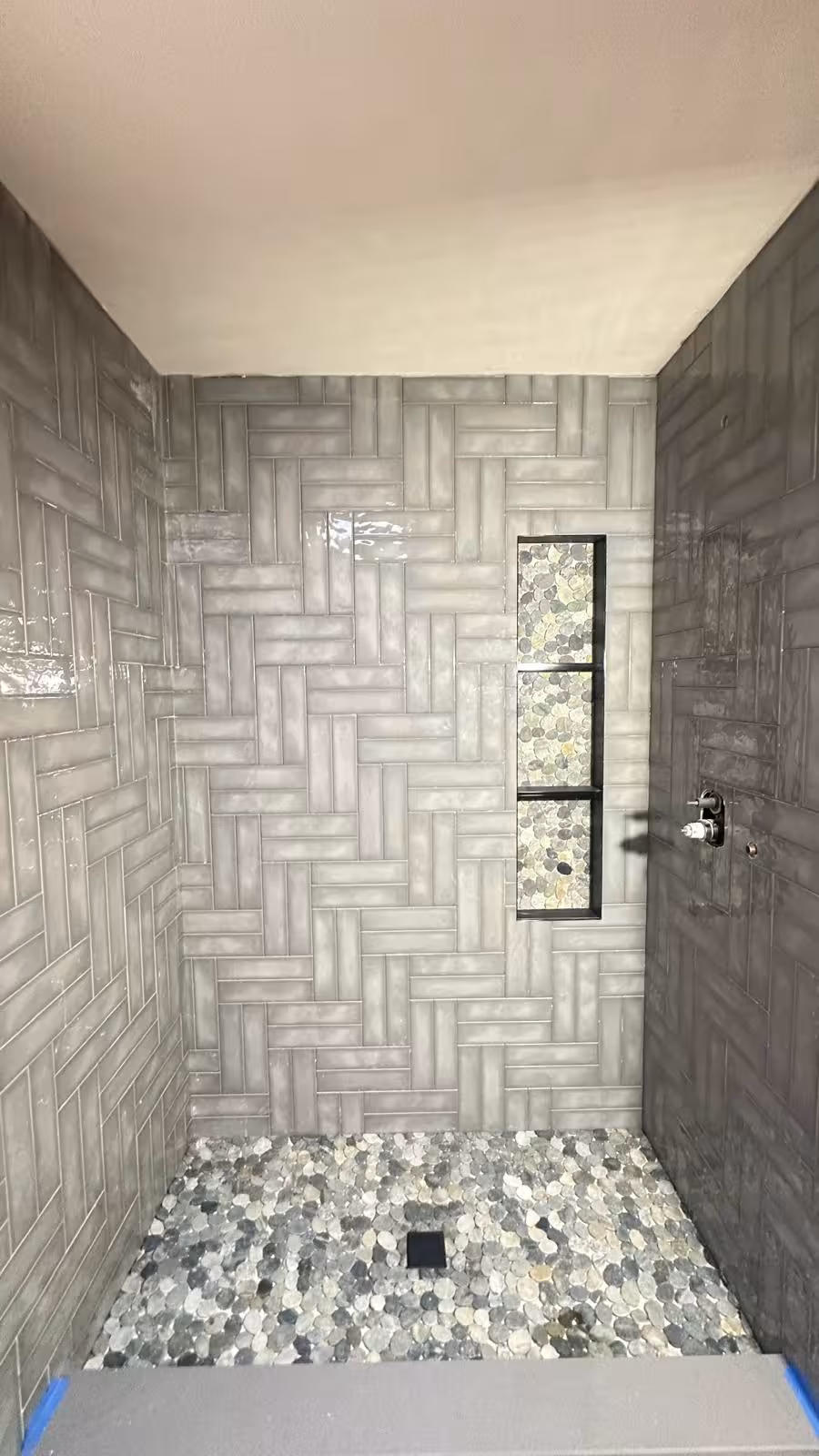 Completed walk-in shower with gray herringbone subway tile walls and river pebble stone floor Littleton CO