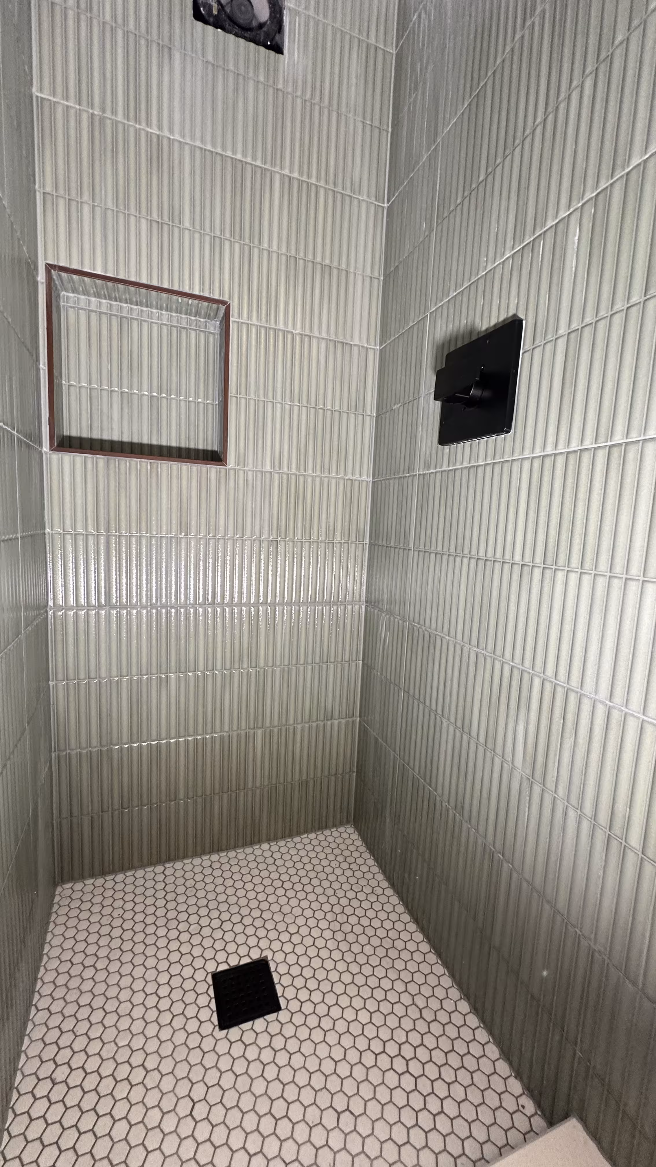 Detail view of the green fluted accent wall with tiled niche and black valve trim in Arvada