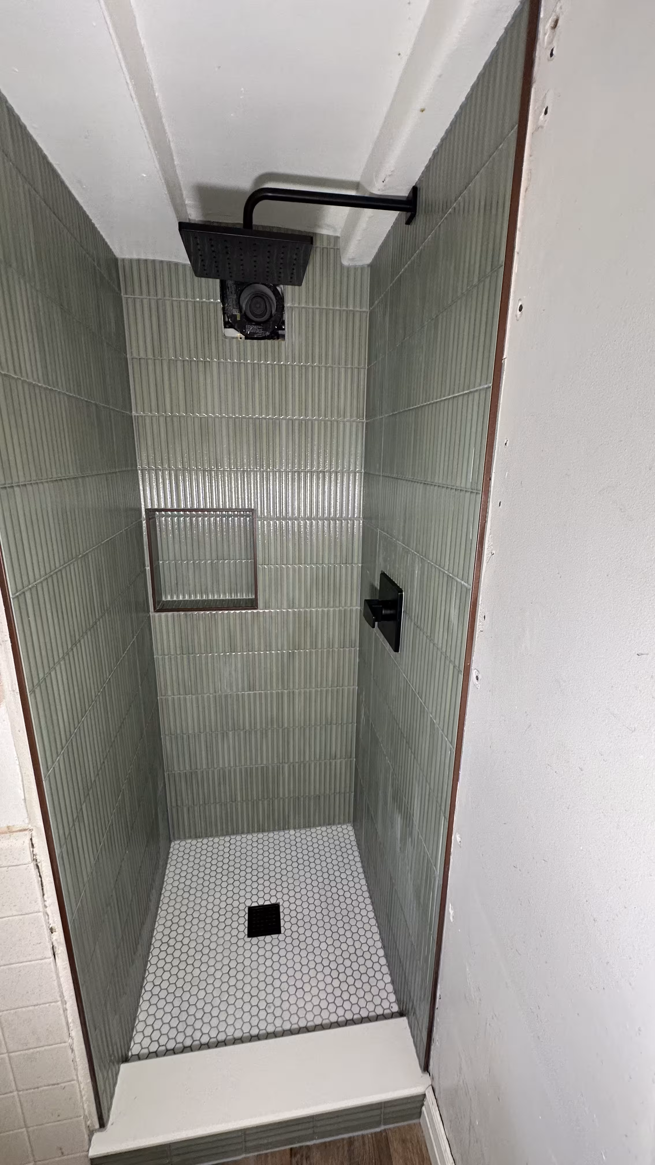 Matte black shower valve trim against green fluted tile with rain shower head overhead in Arvada