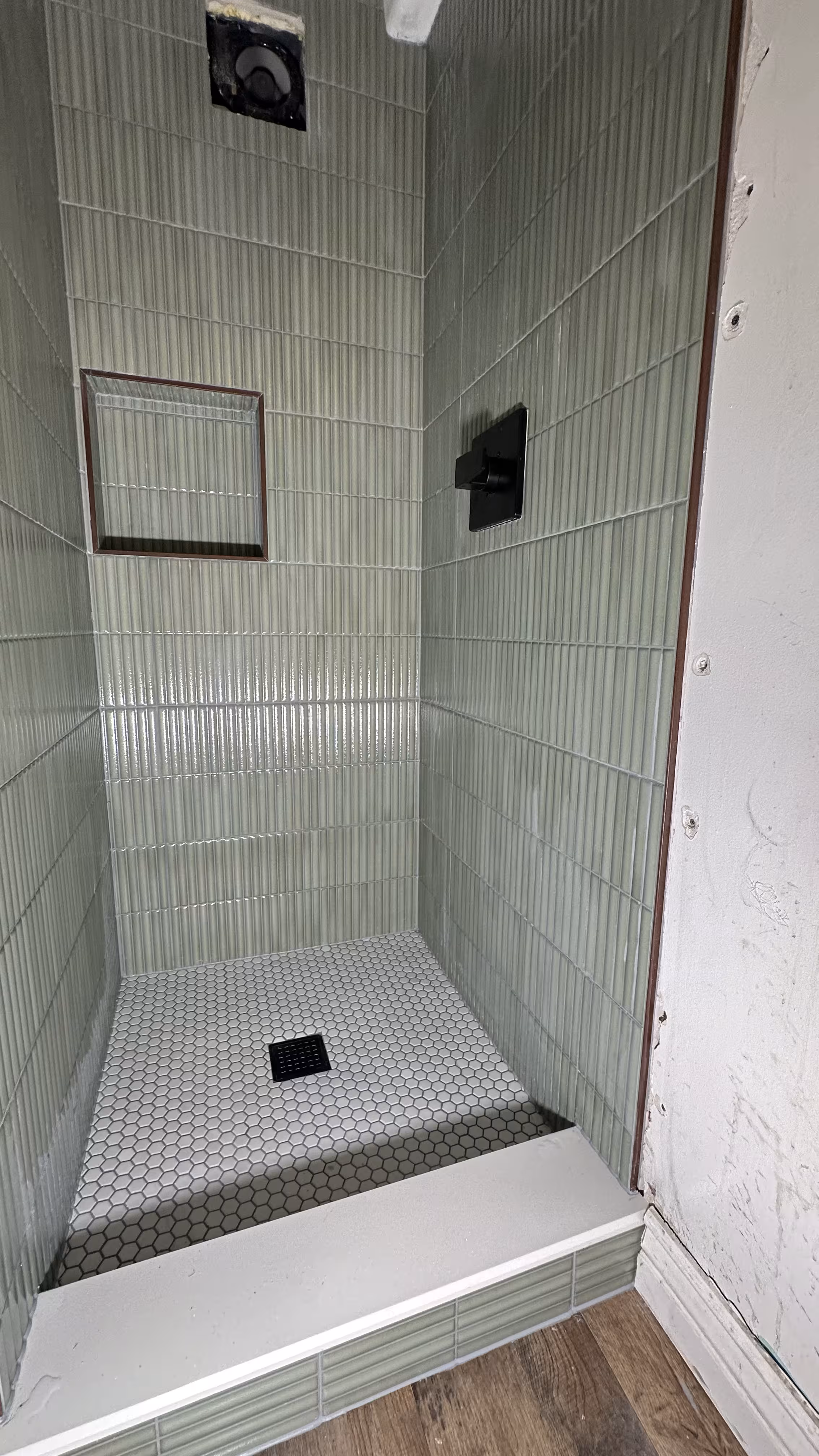 Finished green fluted tile shower with tiled curb opening onto wood flooring in an Arvada bathroom