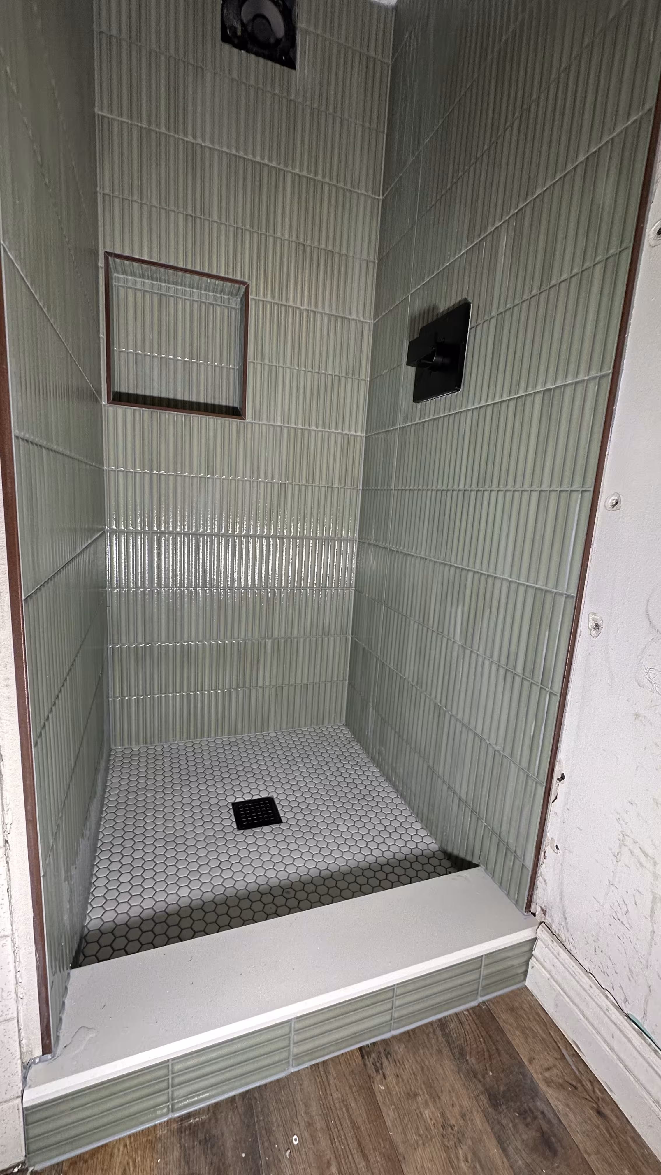 Straight-on view of the completed green fluted tile shower walls and hexagon mosaic floor in Arvada