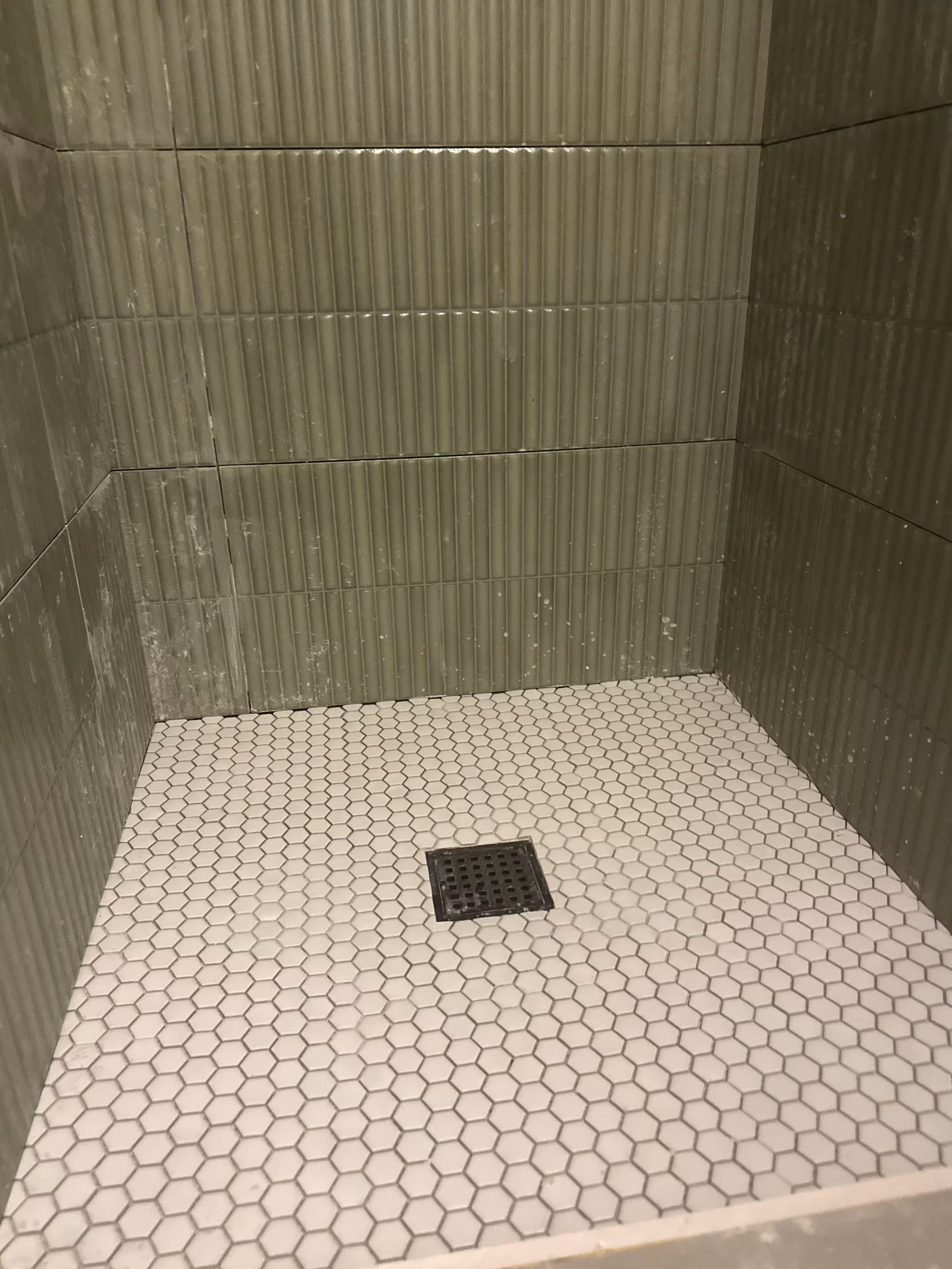 Green fluted tile shower wall and white hexagon floor tile with grout haze before final cleaning in Arvada, CO
