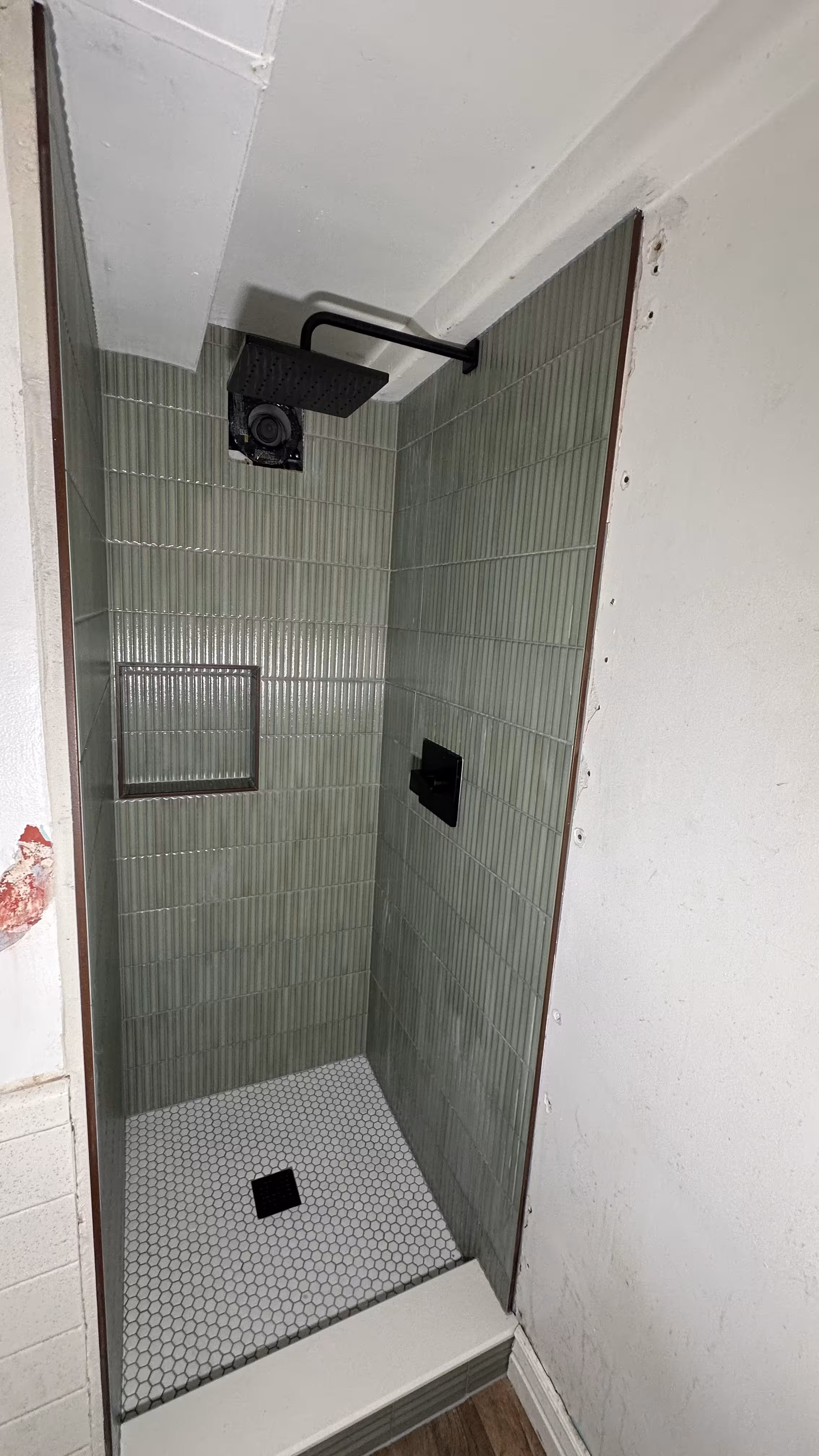 Matte black rain shower head and hand wand mounted above green fluted tile walls in Arvada