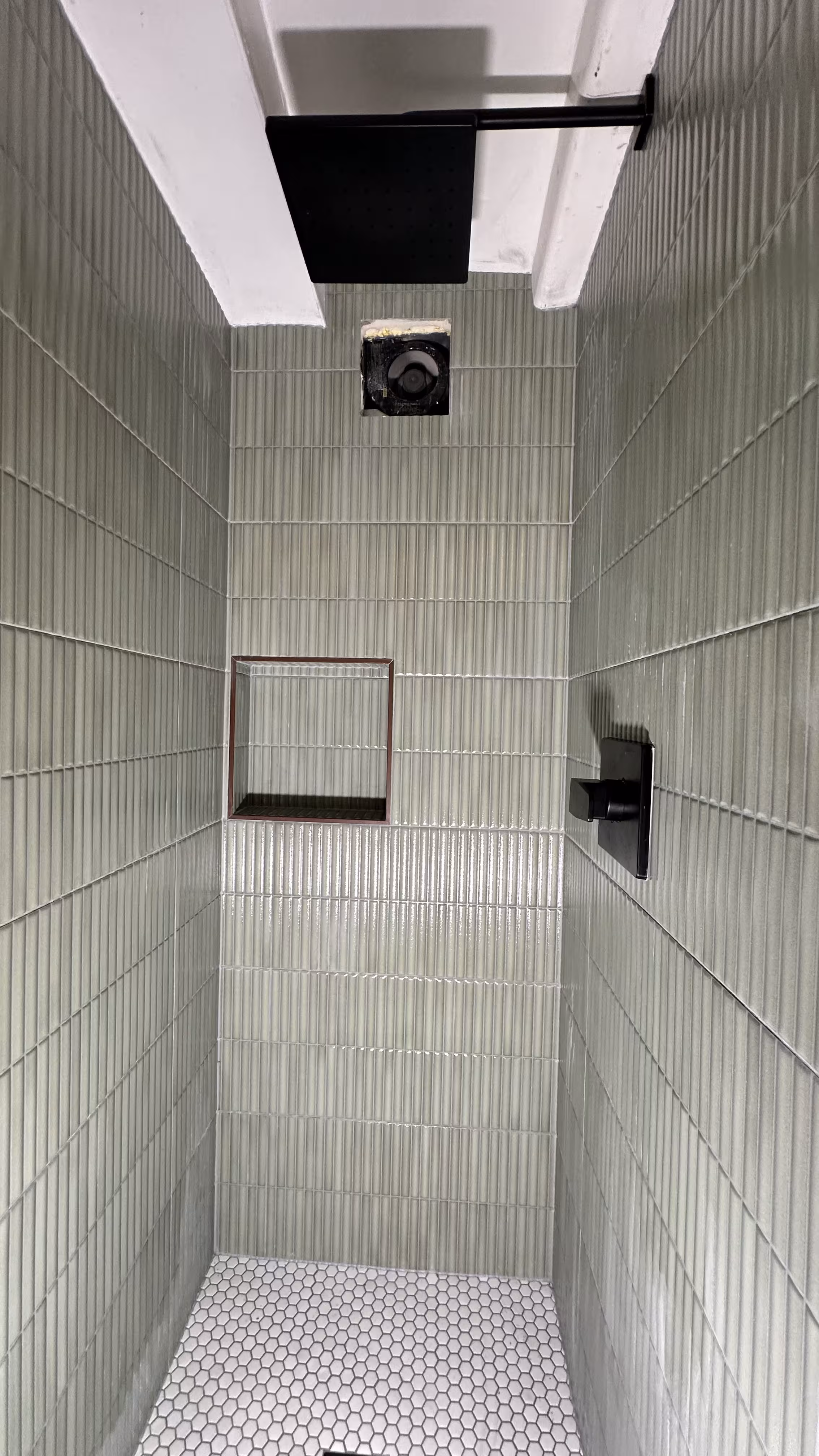 Tall vertical view of the green fluted tile shower from the ceiling beam down to the hexagon floor