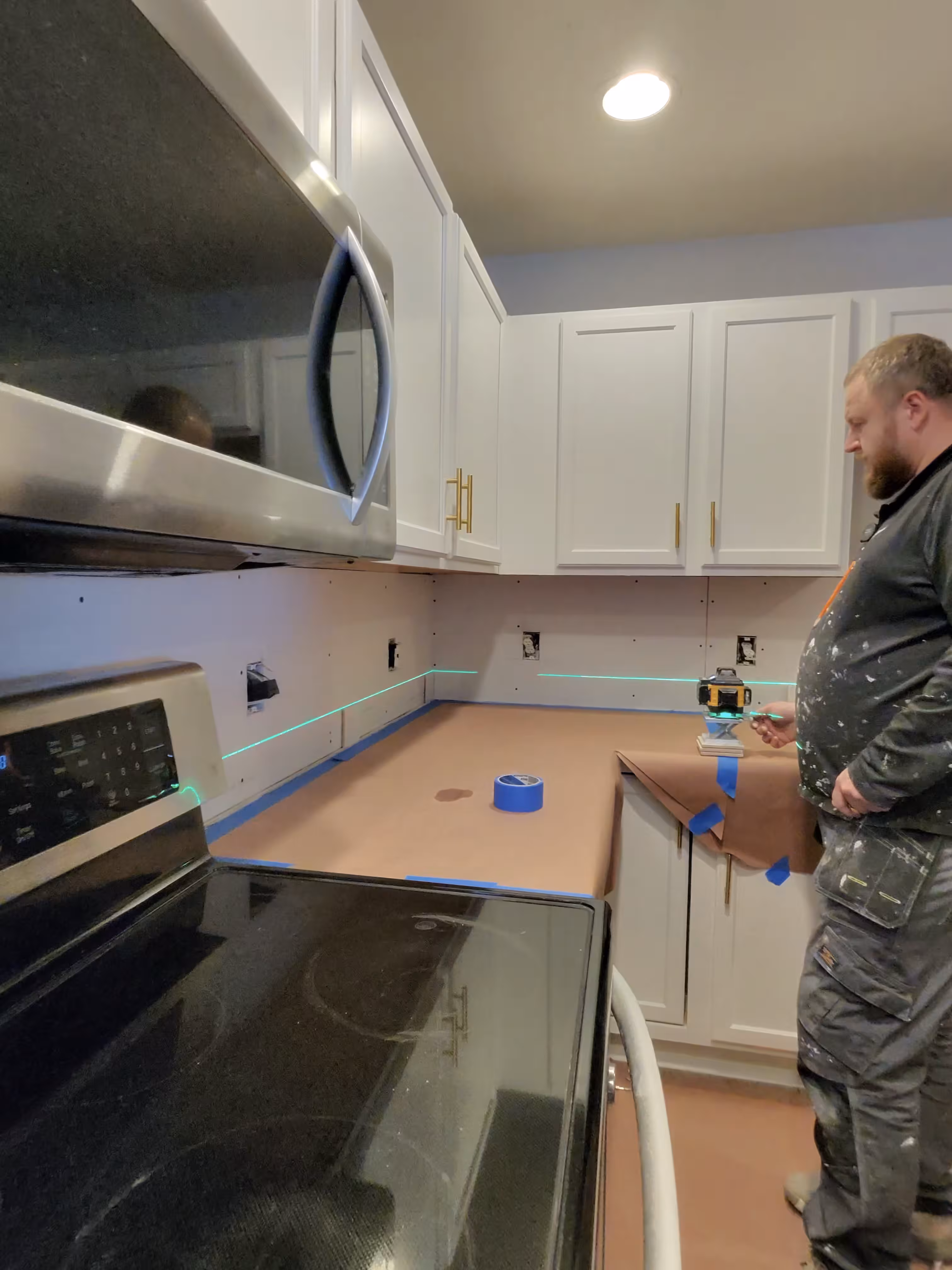 Contractor using a green laser level to lay out level tile lines across bare backer board in this Aurora kitchen
