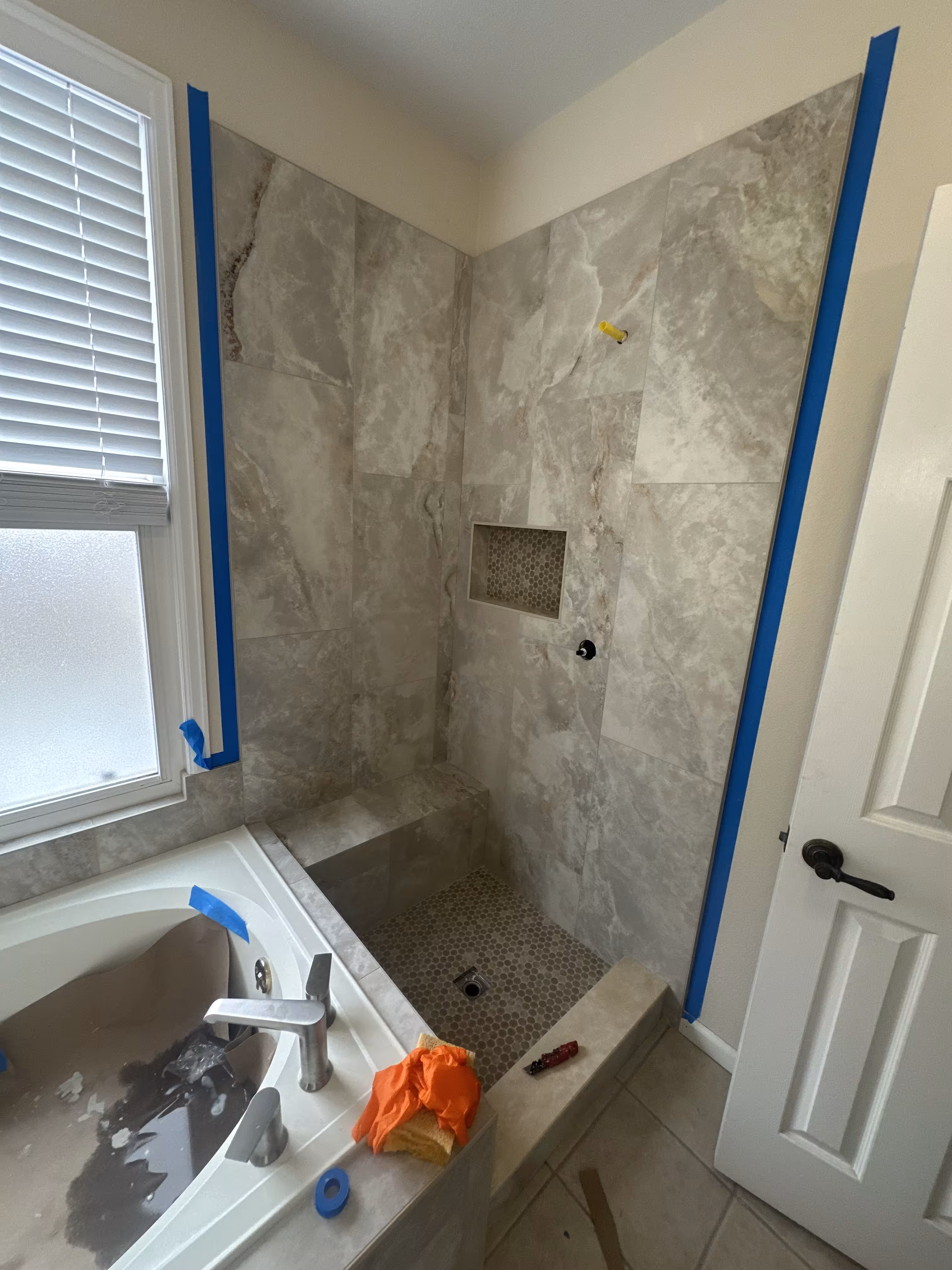 Finished tub and shower corner together showing marble-look tile, penny floor, and chrome faucet in this Highlands Ranch master bathroom