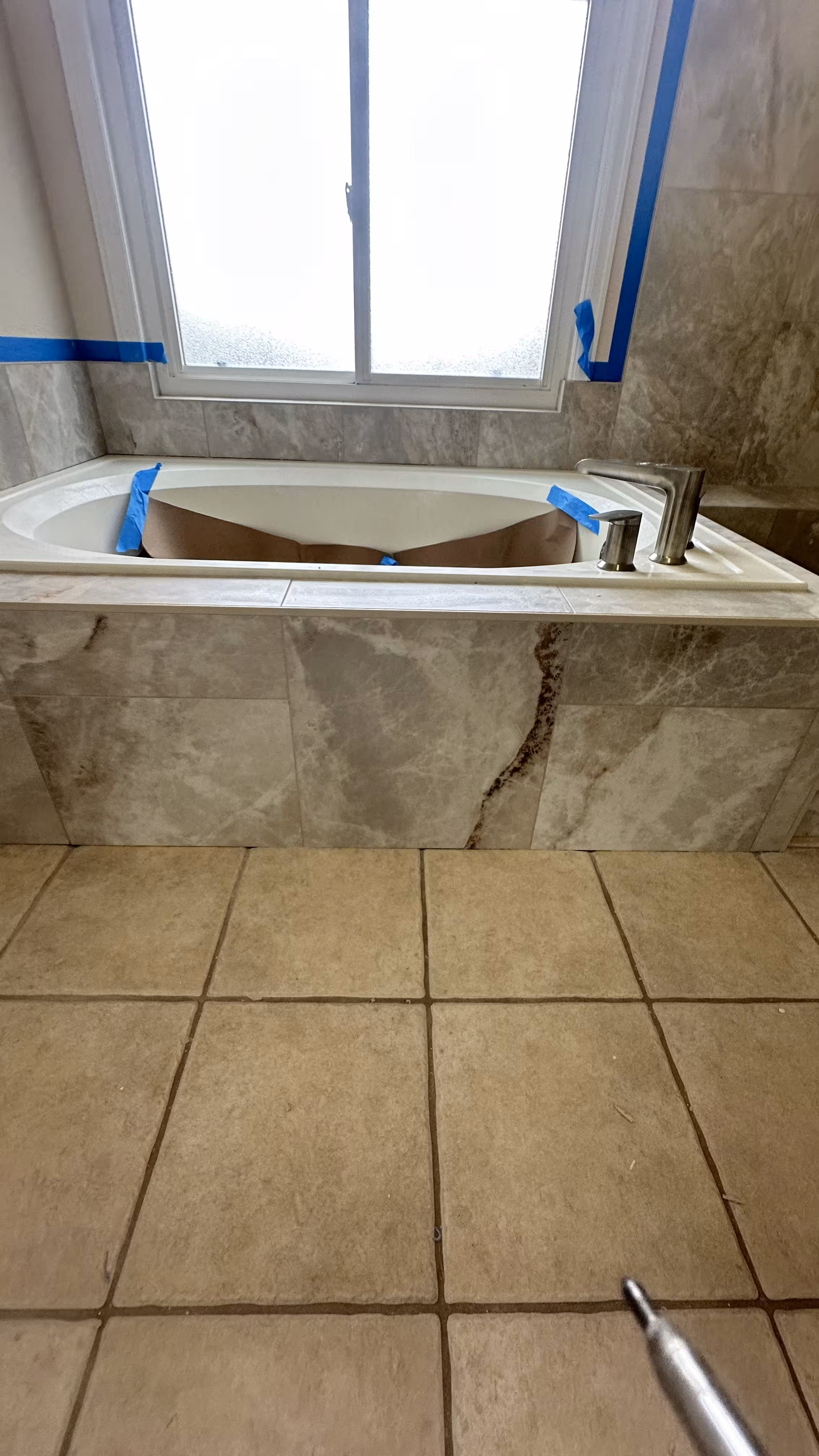 Finished marble-look tub apron tile beneath the window, with beige floor tile in the foreground, Highlands Ranch master bathroom remodel