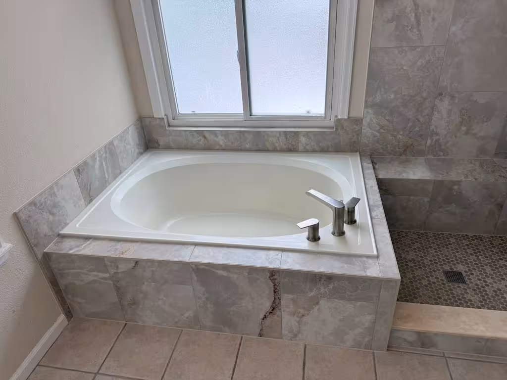 Finished drop-in soaking tub under the window with chrome faucet and marble-look tile apron, Highlands Ranch master bathroom remodel