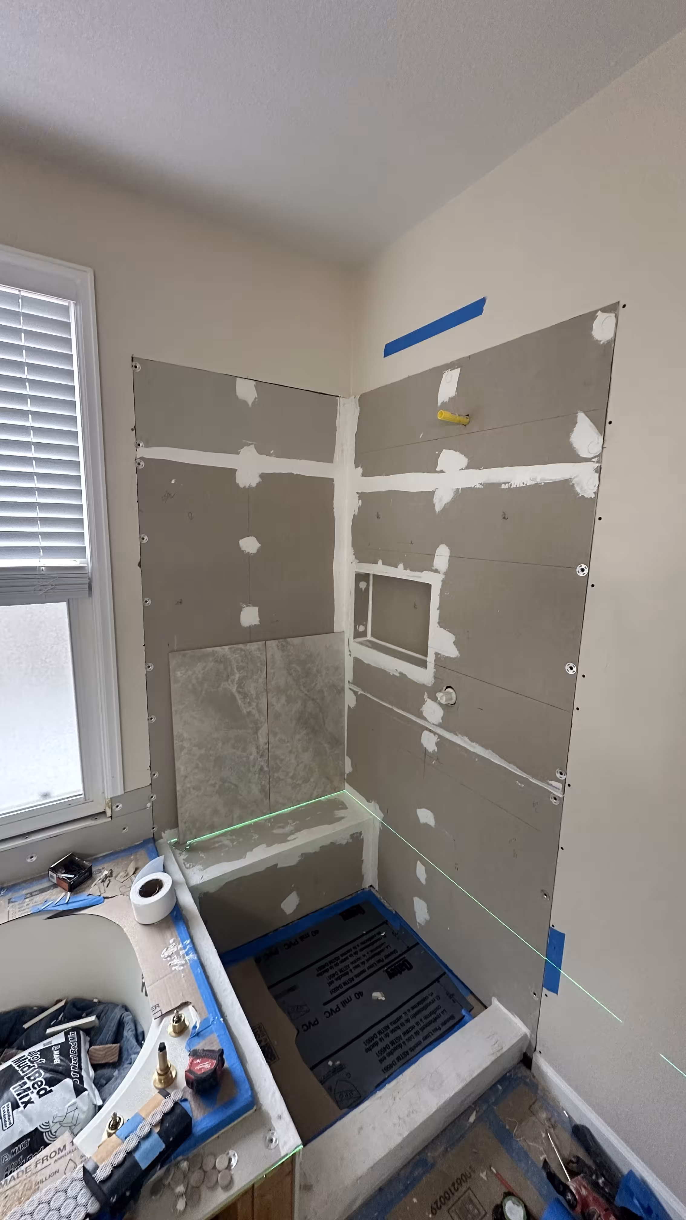 First wall tile course set above the shower bench beside the framed niche, tub, and window during this Highlands Ranch remodel