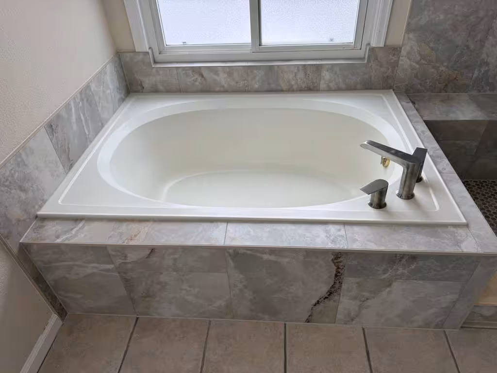 Finished garden-style soaking tub with marble-look tile apron beneath the window in this Highlands Ranch master bathroom remodel