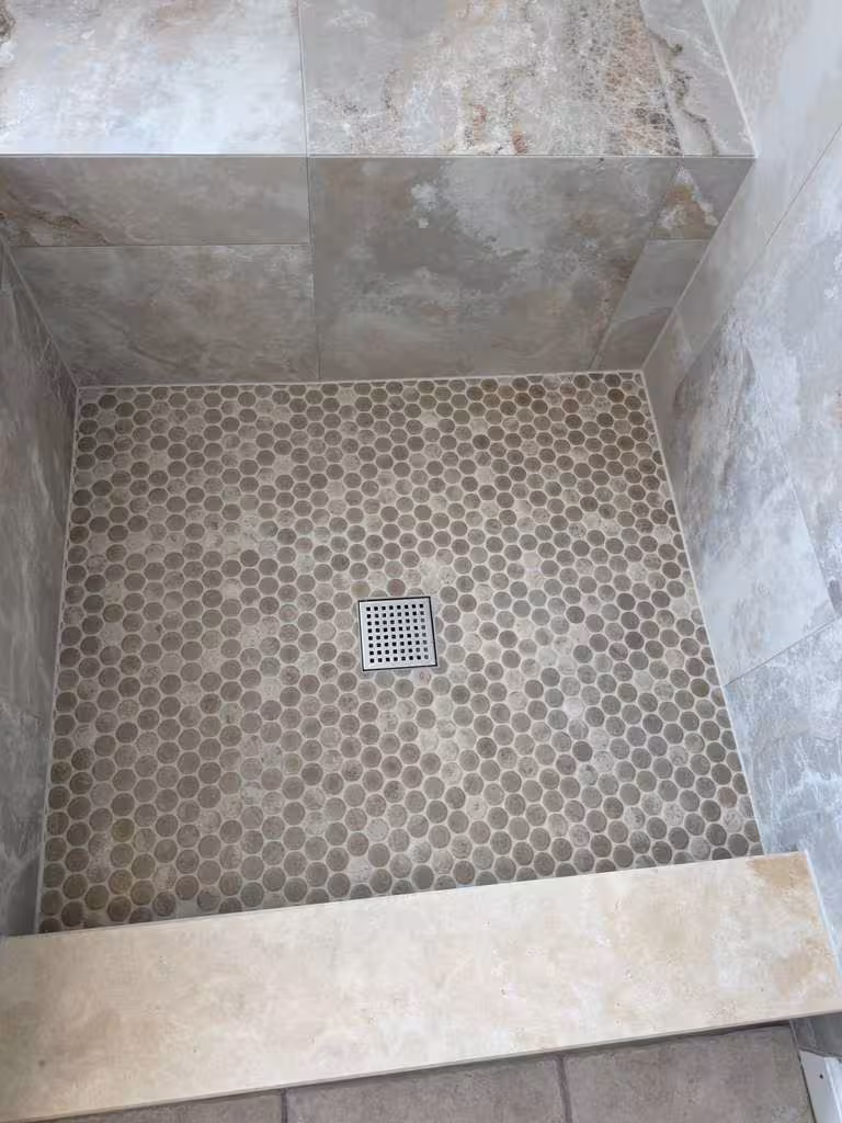 Finished penny-round mosaic shower floor surrounding a square drain, framed by marble-look wall tile in this Highlands Ranch master bath