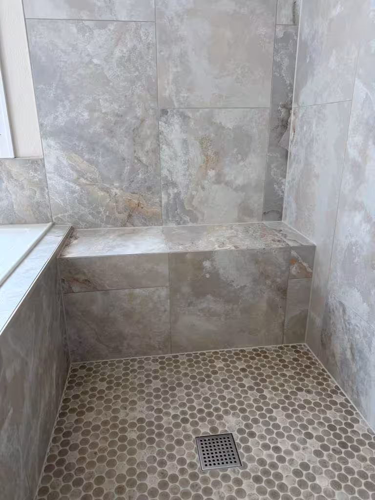 Finished built-in shower bench seat in marble-look tile beside the penny-tile floor and tub edge, Highlands Ranch master bathroom remodel